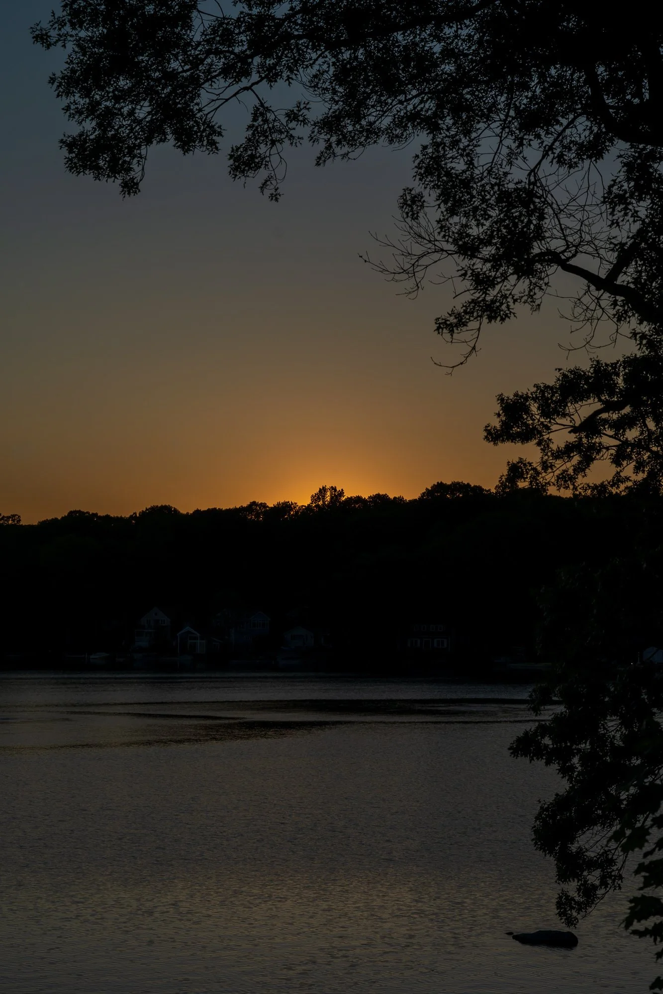 Sunset over Lake Pocotopaug in East Hampton, CT, with silhouettes of trees and houses in the background.