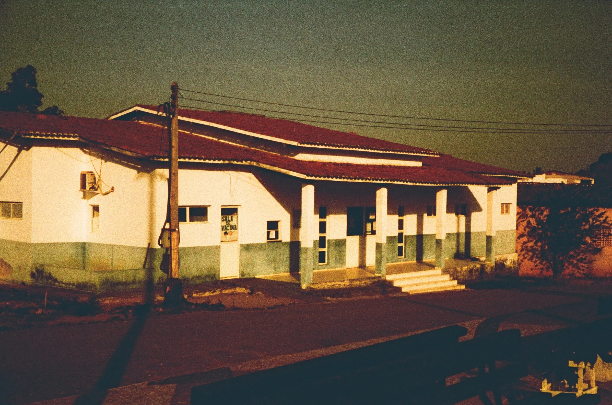 A white house with a red-tiled roof, illuminated by streetlights at night. The house has several windows, a small staircase leading to the front door, and a covered porch supported by columns, located in Ceará, Brazil.