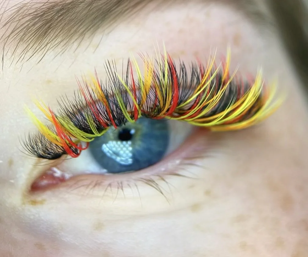 Close-up of a blue eye with colorful eyelash extensions in yellow, red, and black.