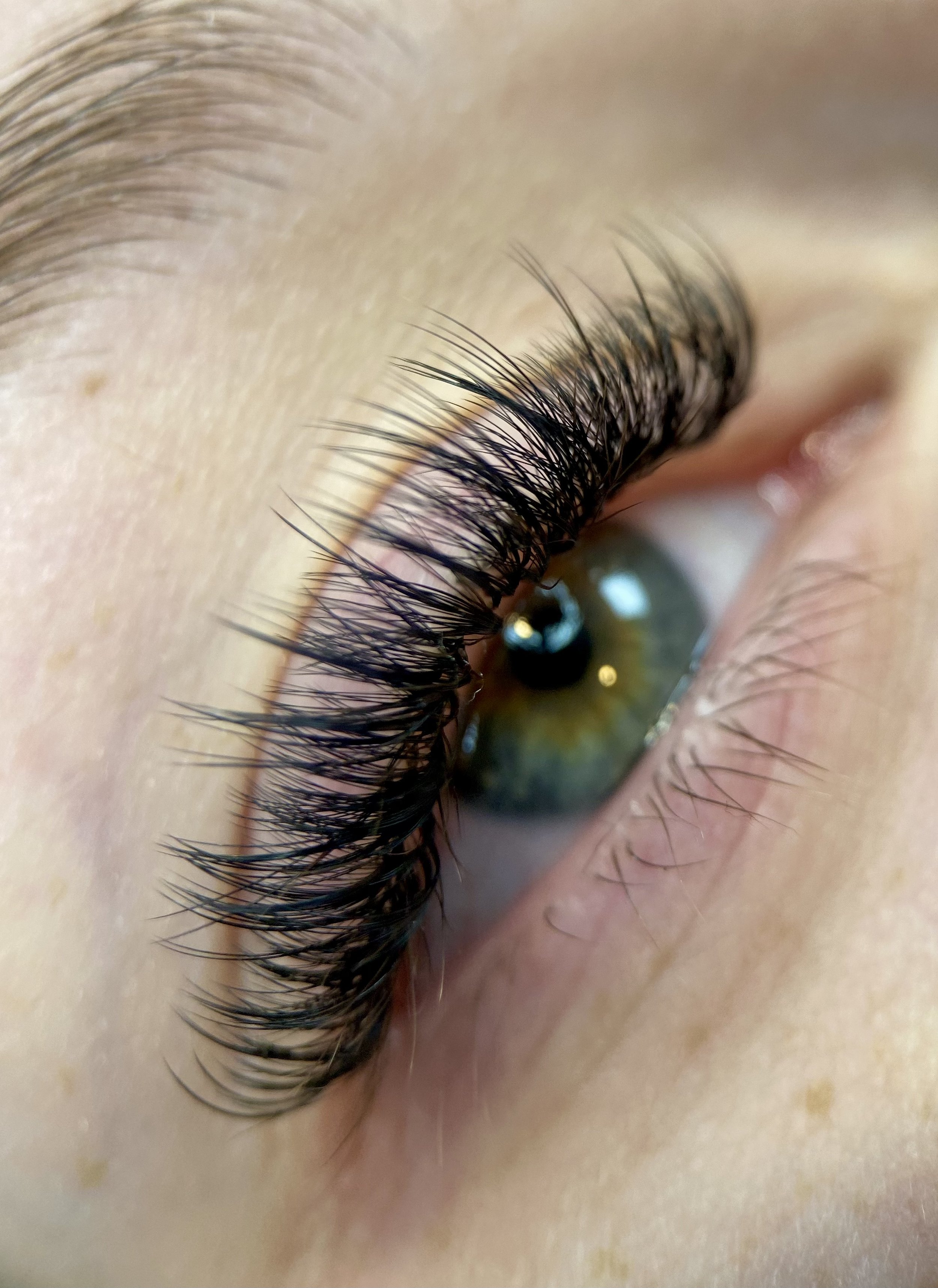 Close-up of a person's eye with long, dark eyelashes and an iridescent green and blue iris.