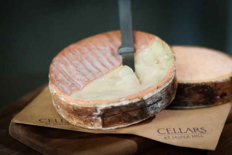 Winnimere, a washed-rind spruce wrapped cheese, with its top rind sliced off revealing it's ivory, custard-like paste