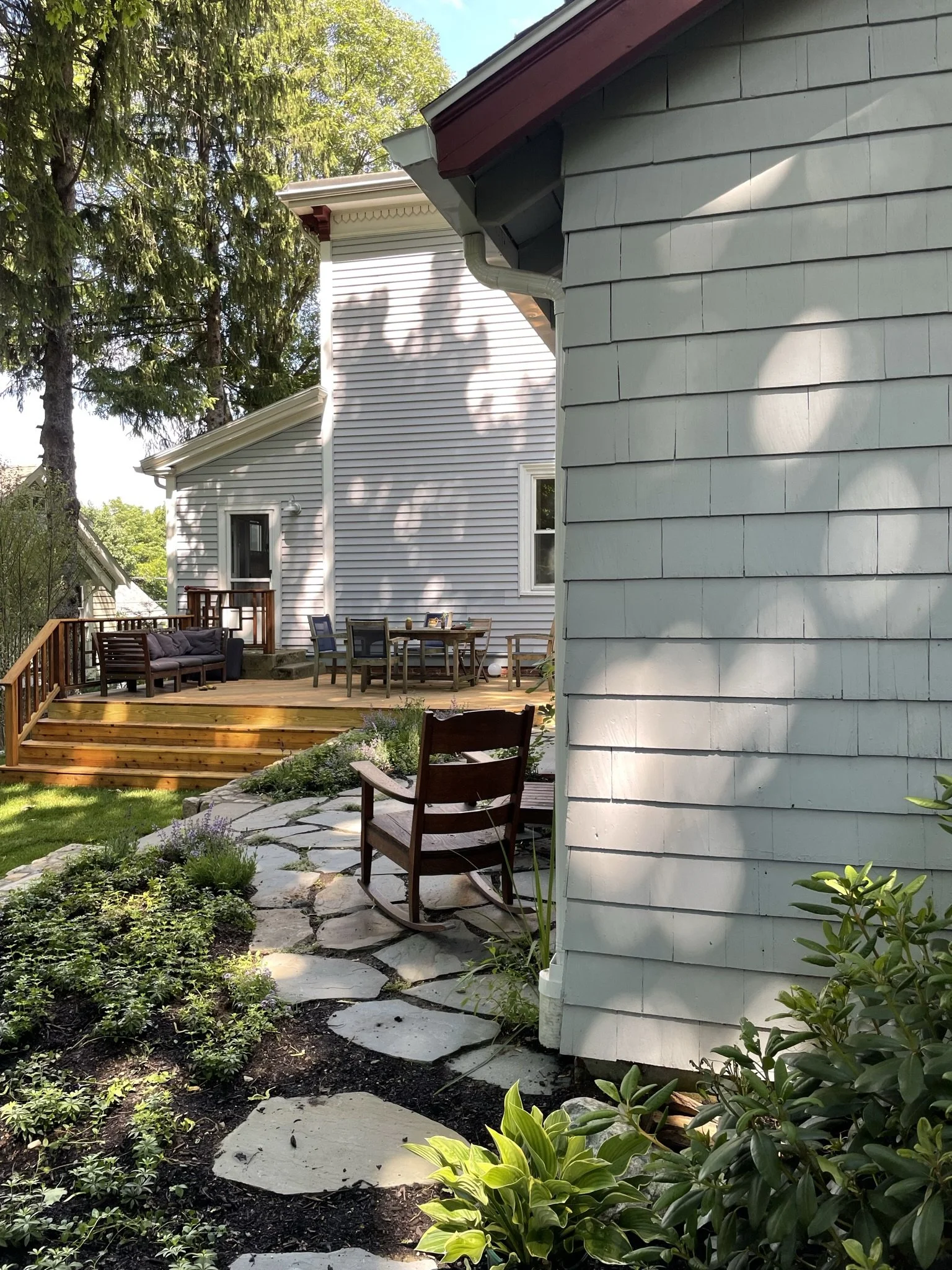 Backyard with a wooden deck, patio furniture, and garden path lined with plants.