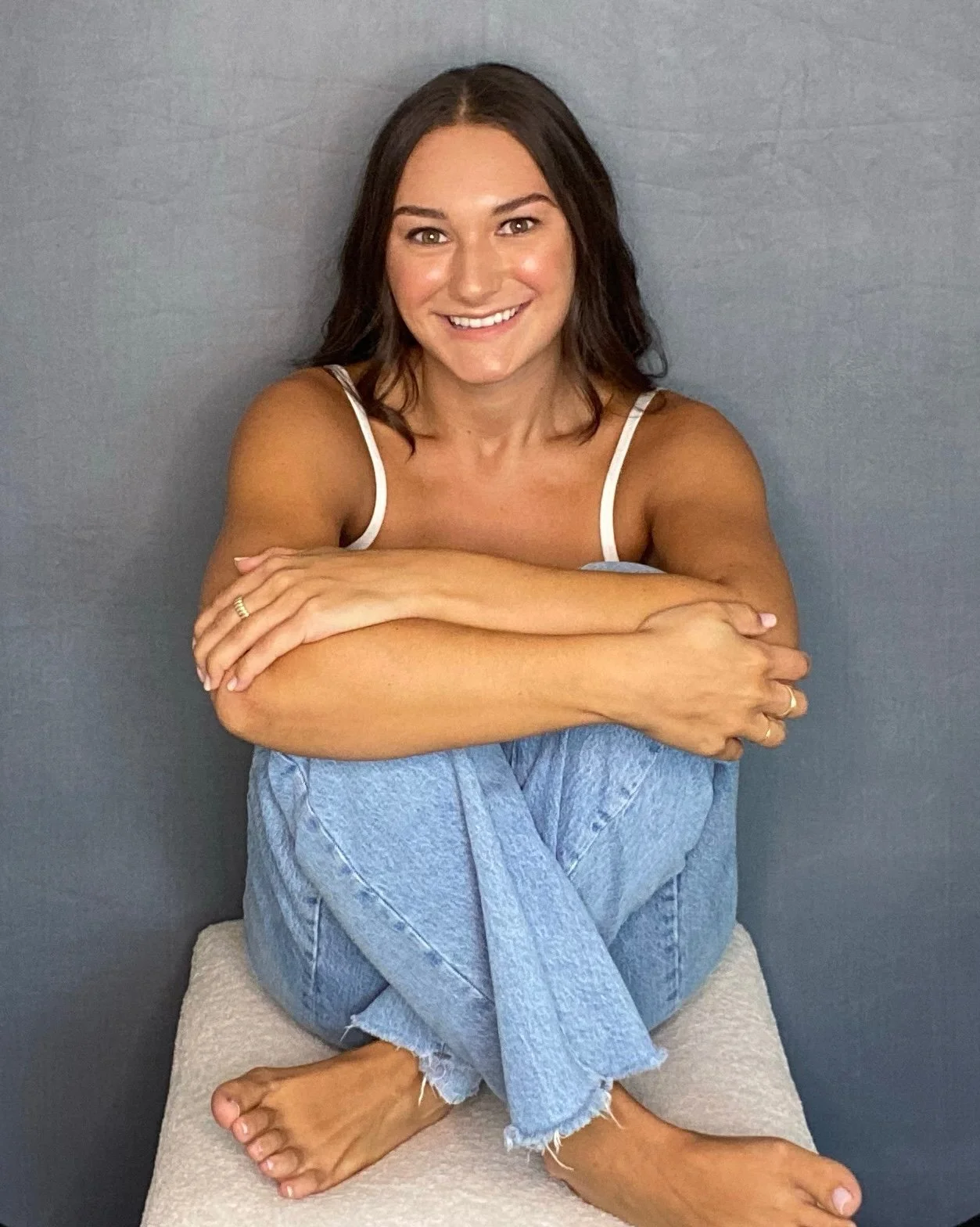 Theatre, TV, and film actress Abby Rae Marcus sits on a stool with her knees to her chest as she poses with a big smile. Paul Smith Photography.