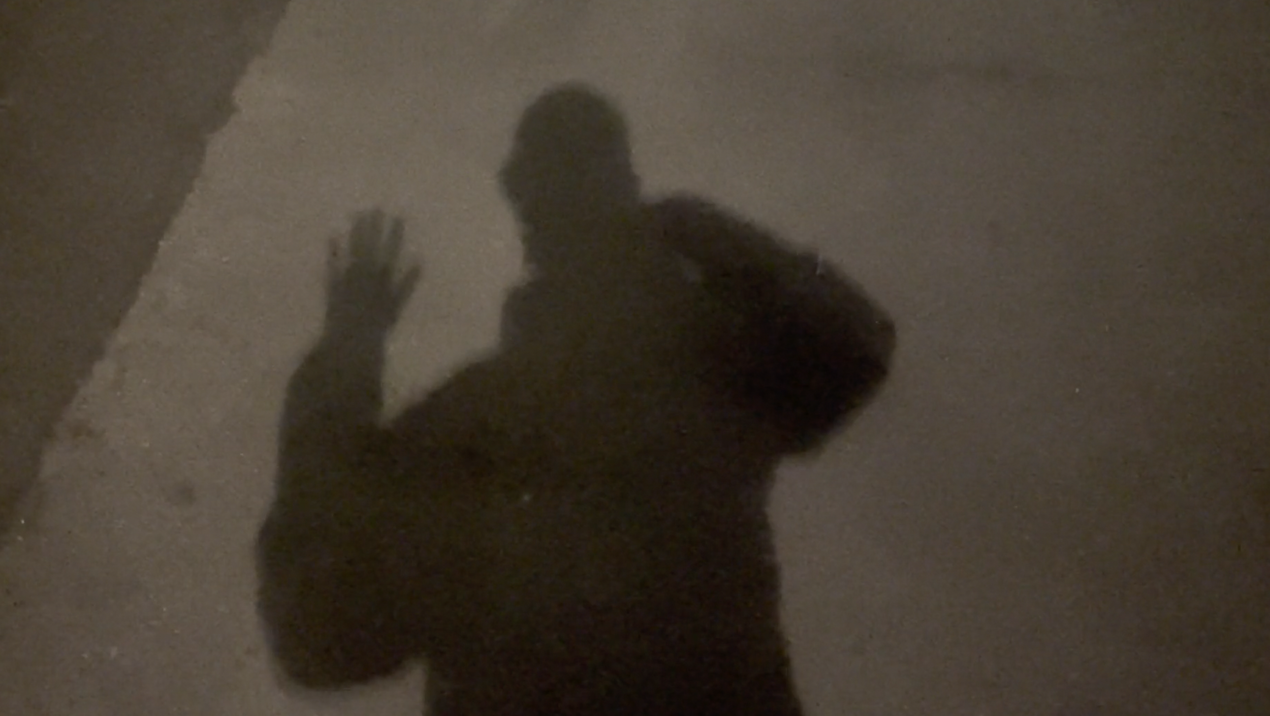 Shadow of a person on a concrete wall, waving with one hand, holding a backpack on their shoulder.