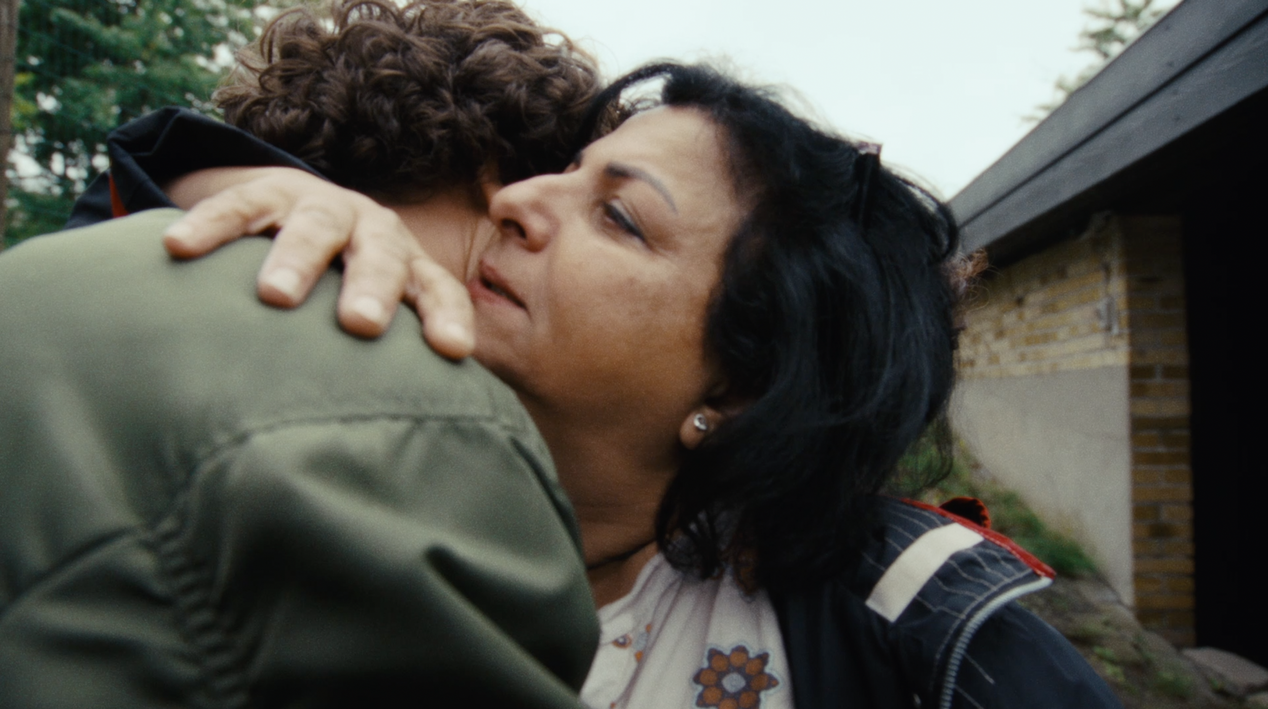 Two women embracing each other outdoors, with the woman on the right appearing emotional.