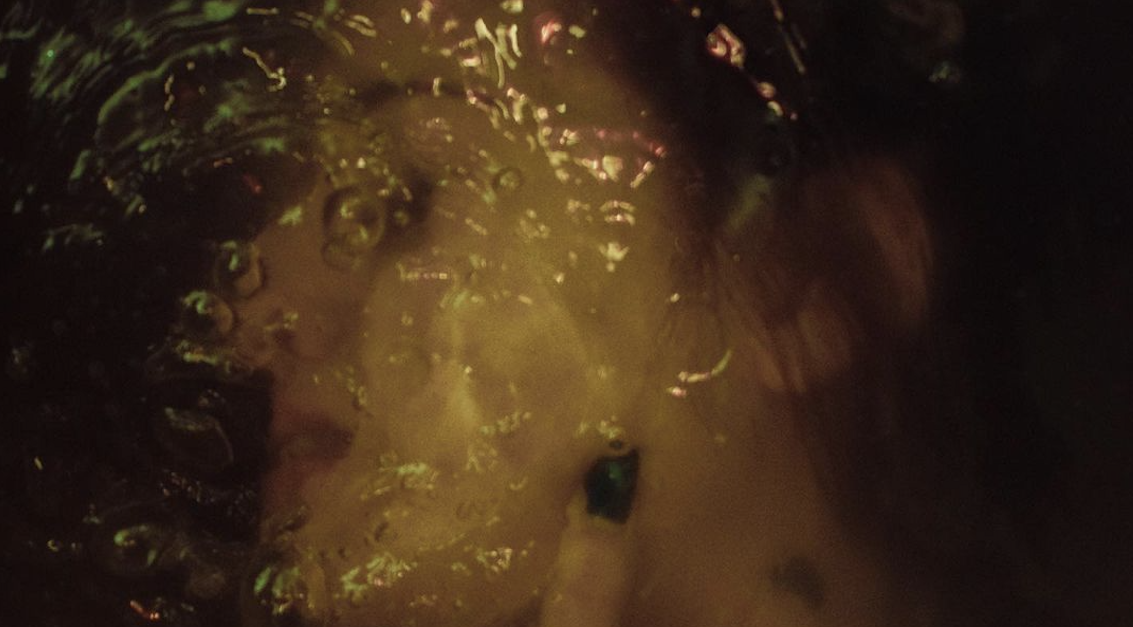 Close-up of bubbling liquid with dark and yellowish hues, possibly in a pot or container, with reflections and bubbles surface.