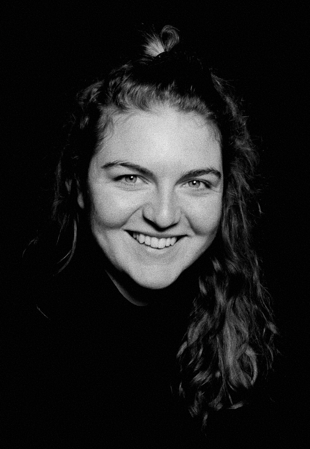 Black and white portrait of a smiling woman with long wavy hair, looking directly at the camera.