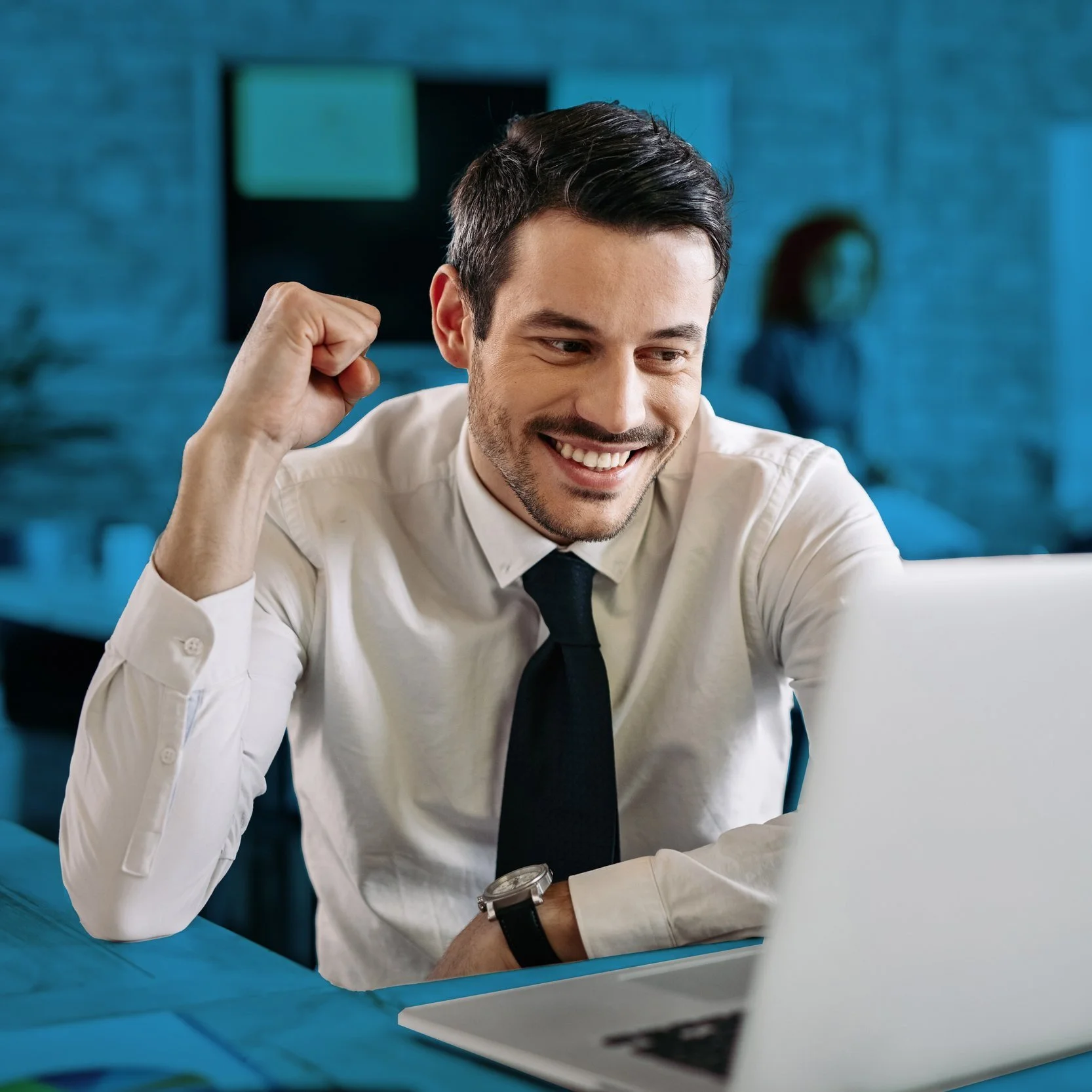Hombre de negocios celebrando con una sonrisa y el puño en señal de victoria frente a una computadora portátil en una oficina moderna