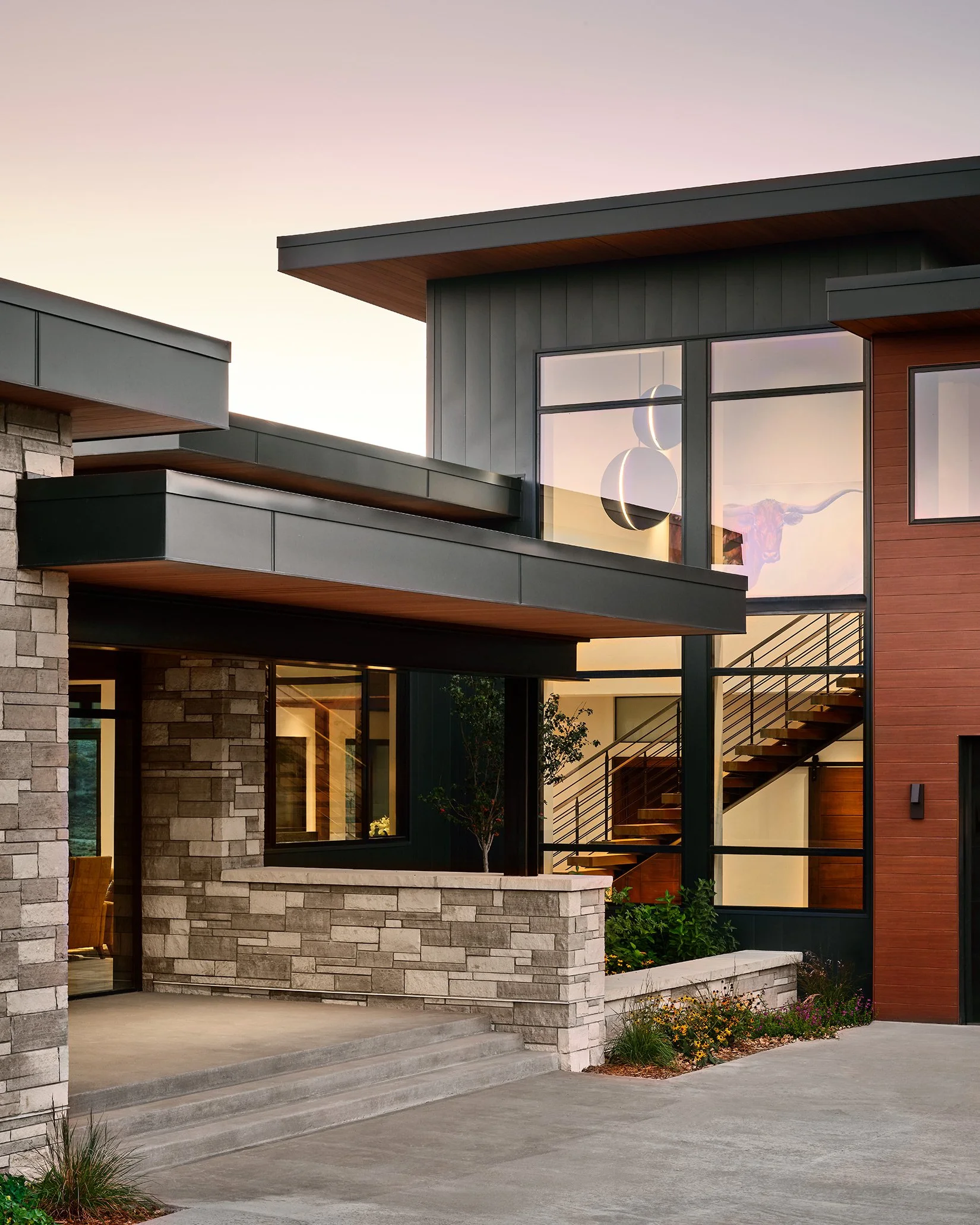 Modern house with stone, wood, and large glass windows at sunset