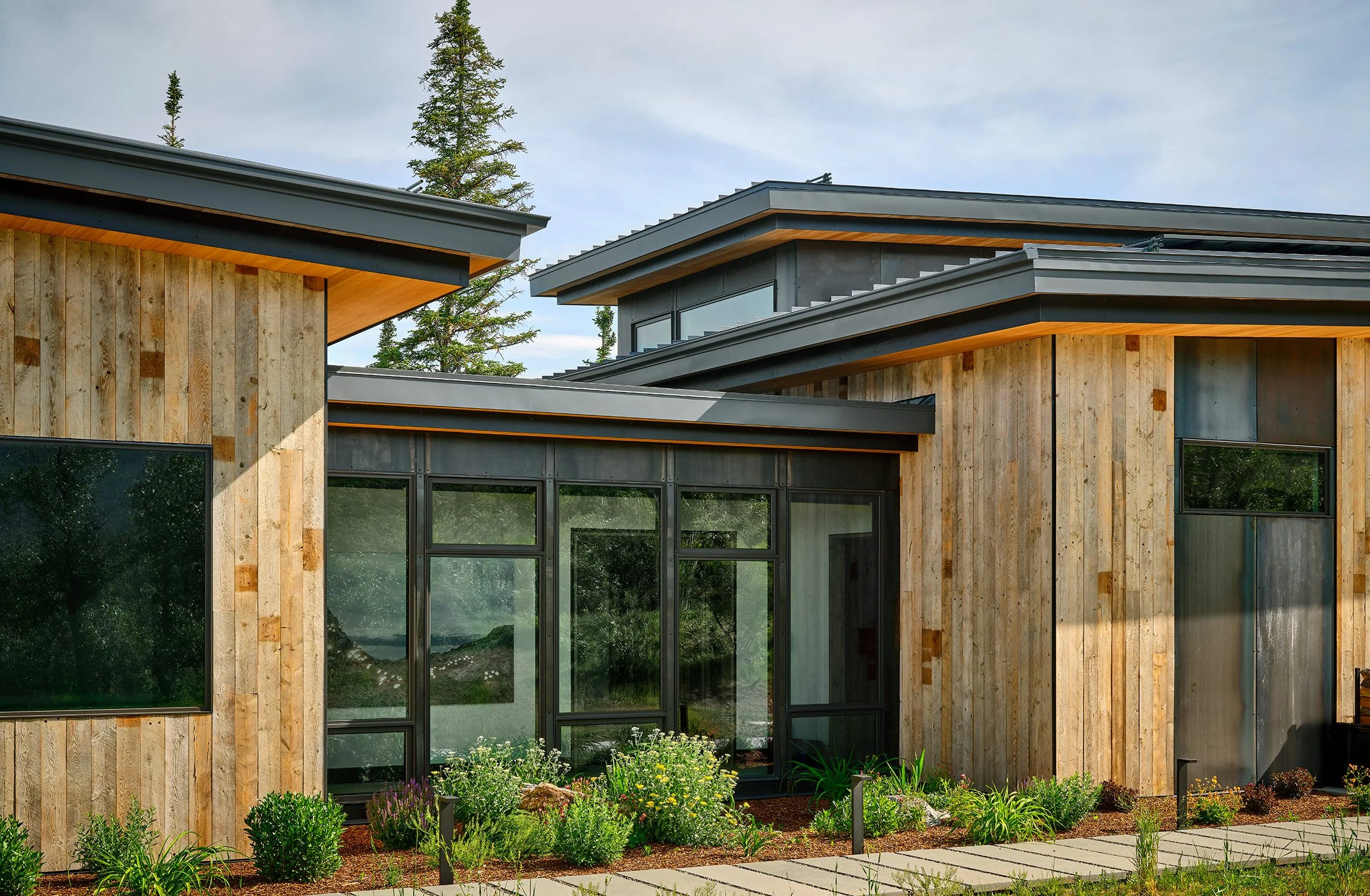 Modern house with wooden siding, large glass windows, and a garden with plants and flowers.