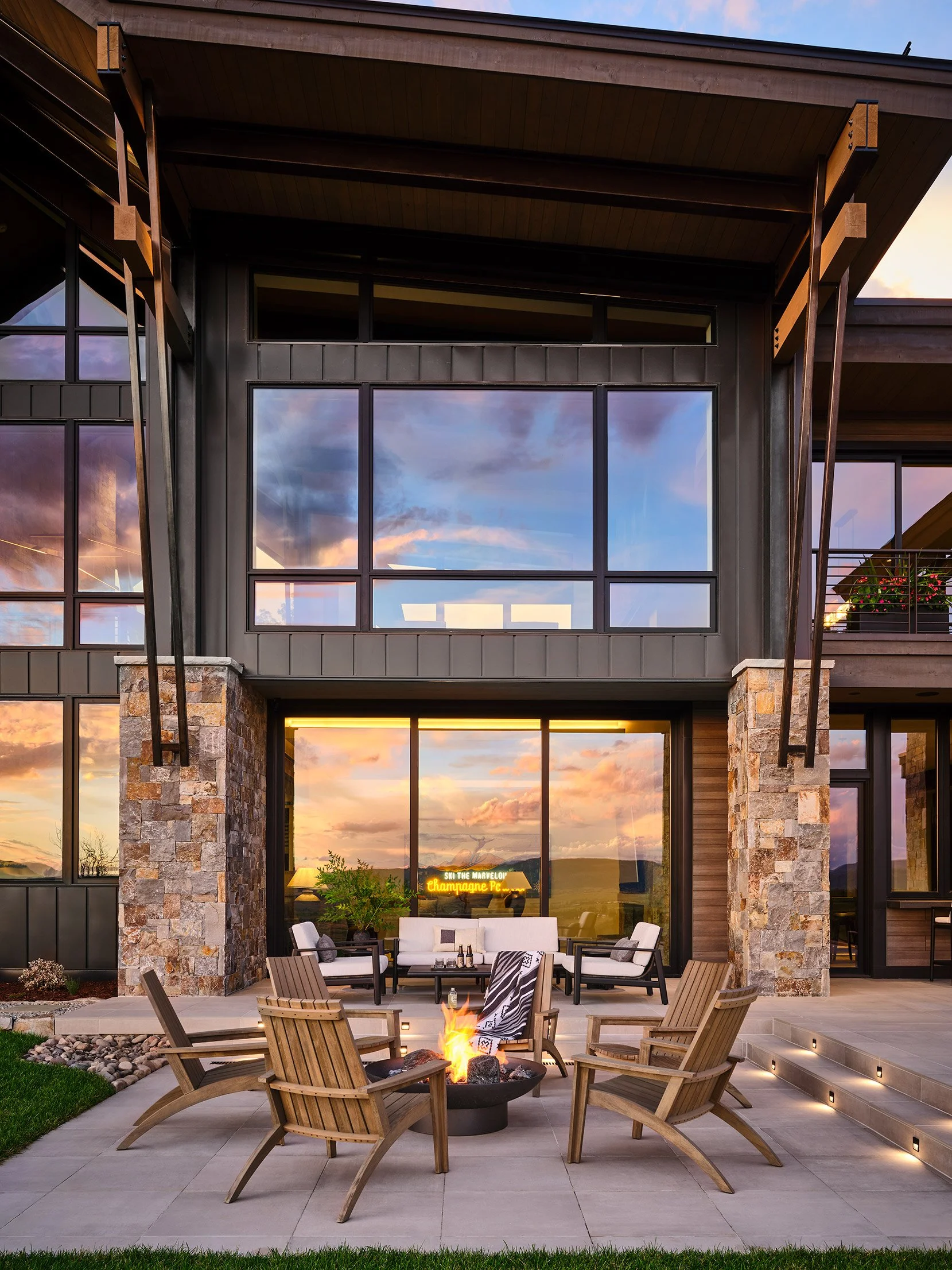 modern house with large windows, outdoor patio with seating and fire pit during sunset.