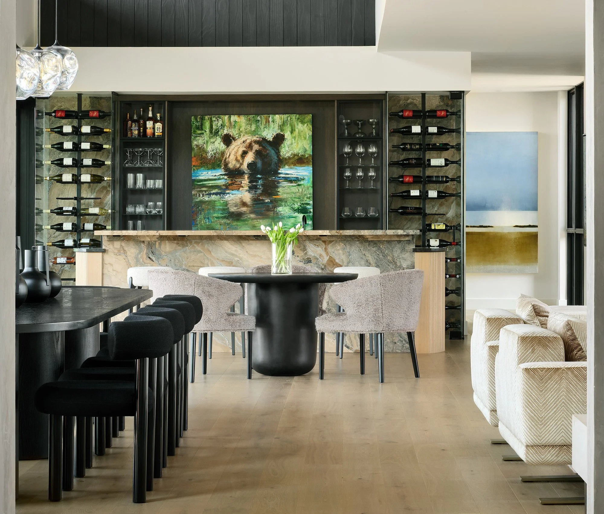 Interior of a modern dining room with a bar area, wine racks, dining table, chairs, and abstract artwork