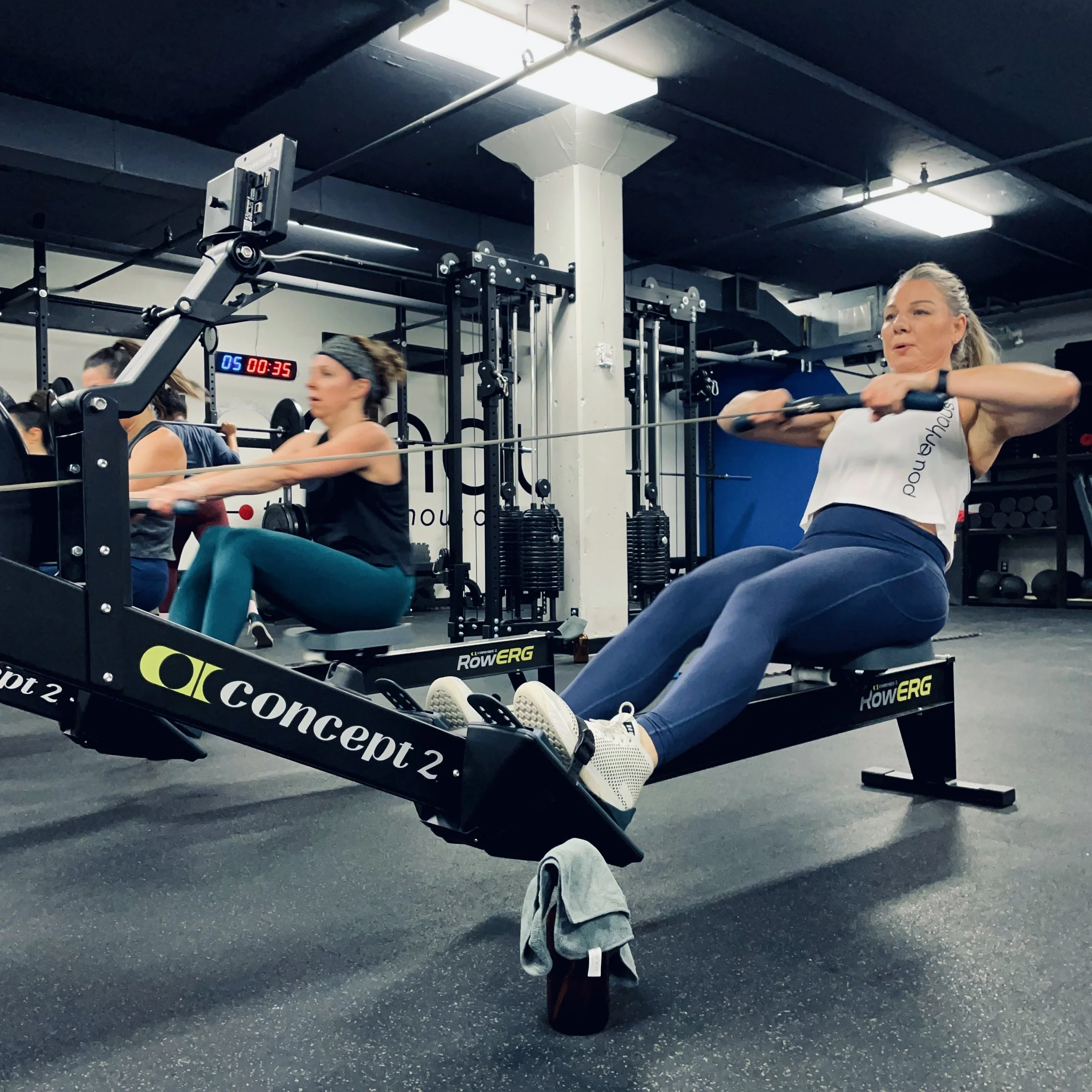 Two women exercising on rowing machines in a gym.