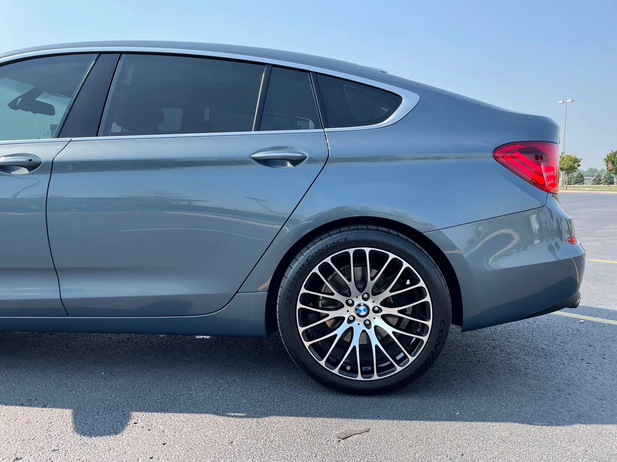 Blue BMW sedan parked in an open lot during daytime, with a clear sky and some trees in the background.