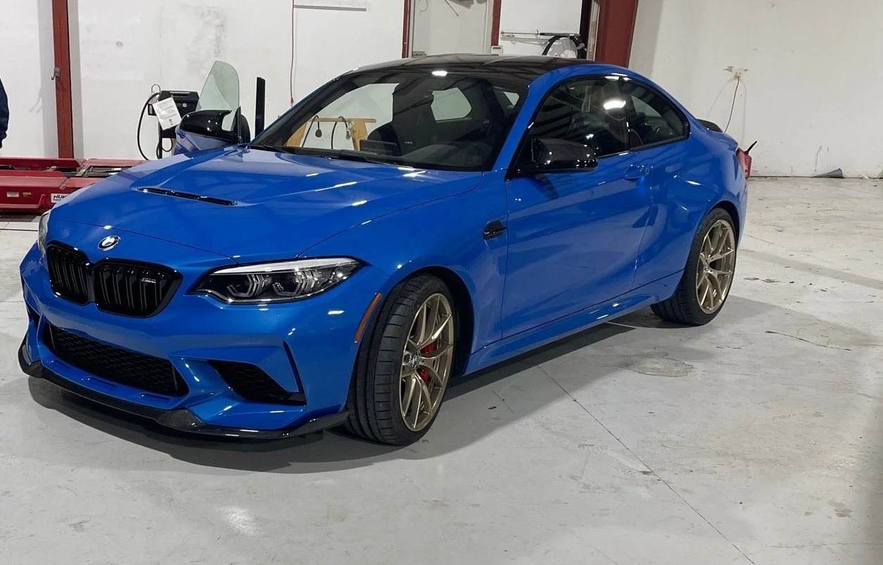 A blue BMW sports car parked in an indoor garage, featuring black accents and gold wheels.
