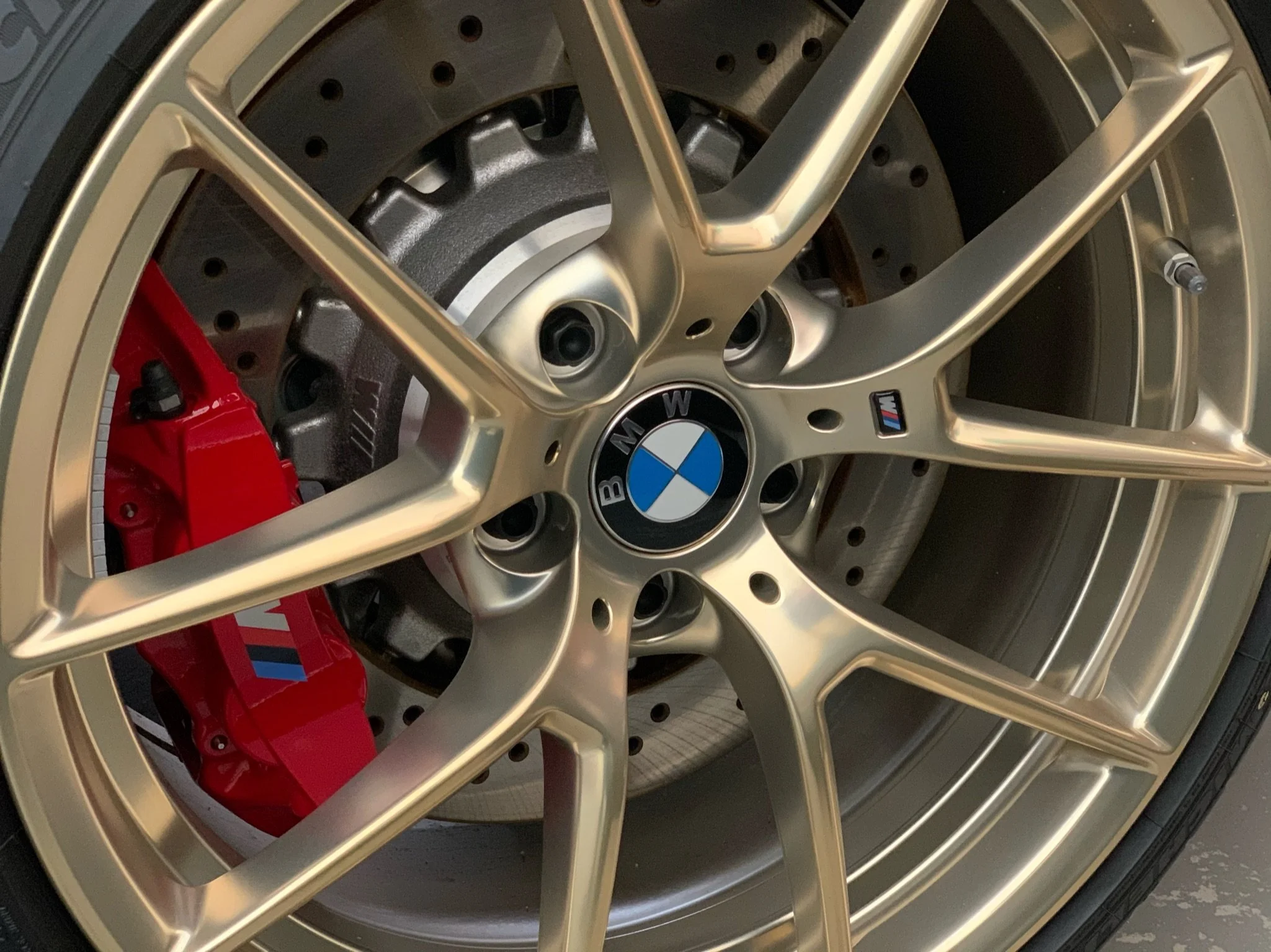 A close-up of a car wheel with a gold rim, red brake caliper, and a BMW M badge.