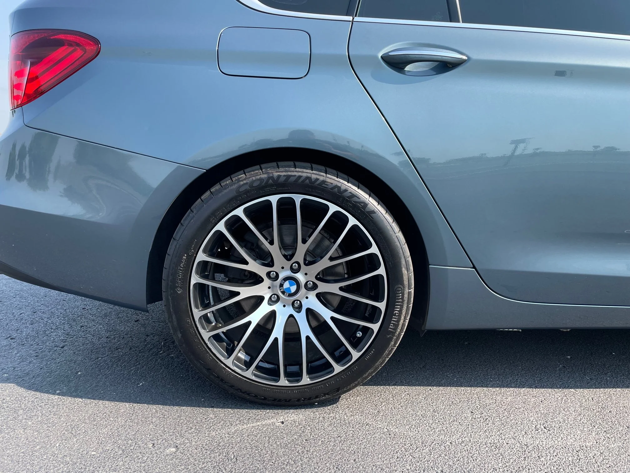 Close-up of a blue BMW car with alloy wheels, parked on asphalt.