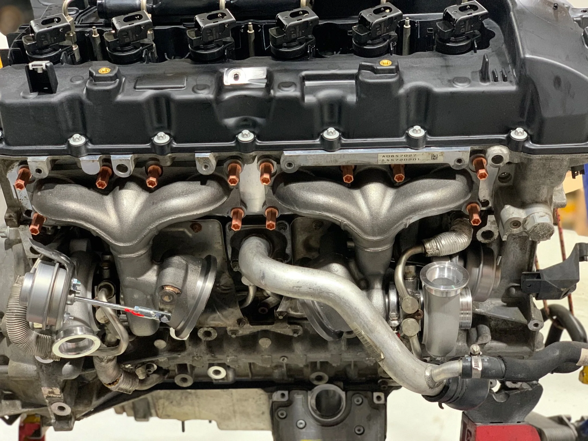 Automobile engine with various metal and plastic components, including hoses, bolts, and fittings, mounted on a workbench or stand.