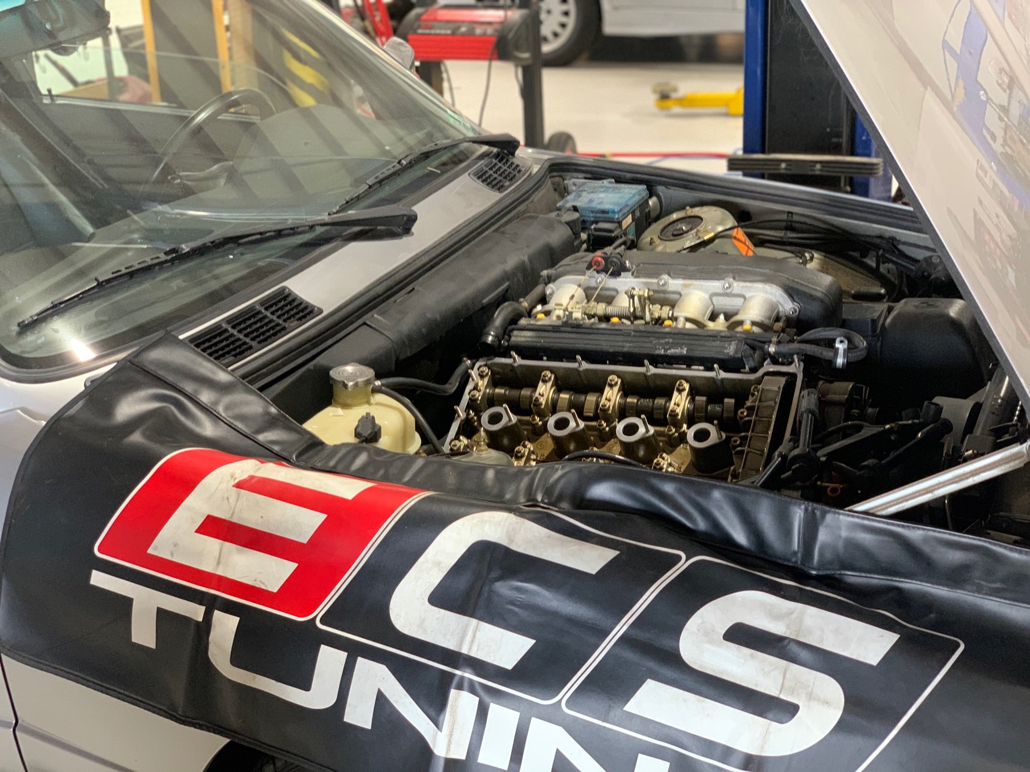 Close-up of a race car with the hood open, showing the engine inside the engine bay and racing decals on the car's body.