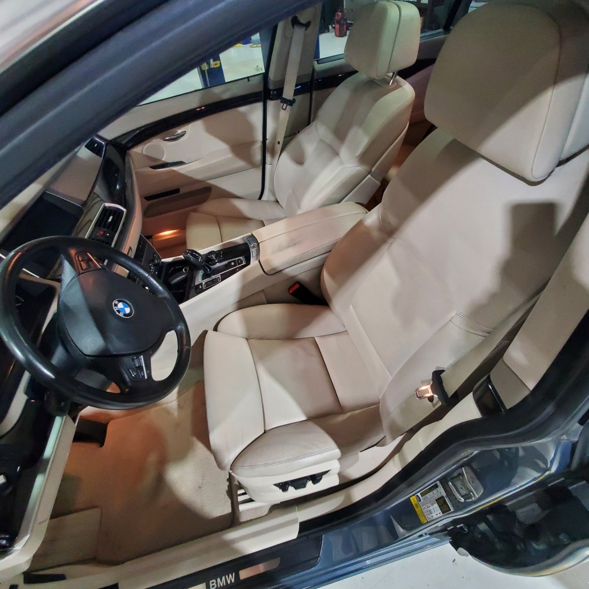 Interior of a BMW car with beige leather seats and dashboard, showing the front seats, steering wheel, and center console.