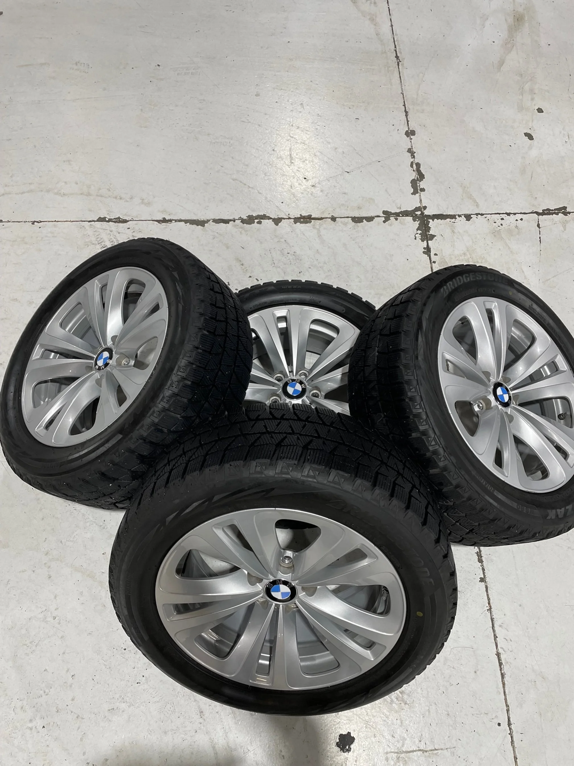 Four BMW alloy wheels with tires, arranged on a concrete floor.
