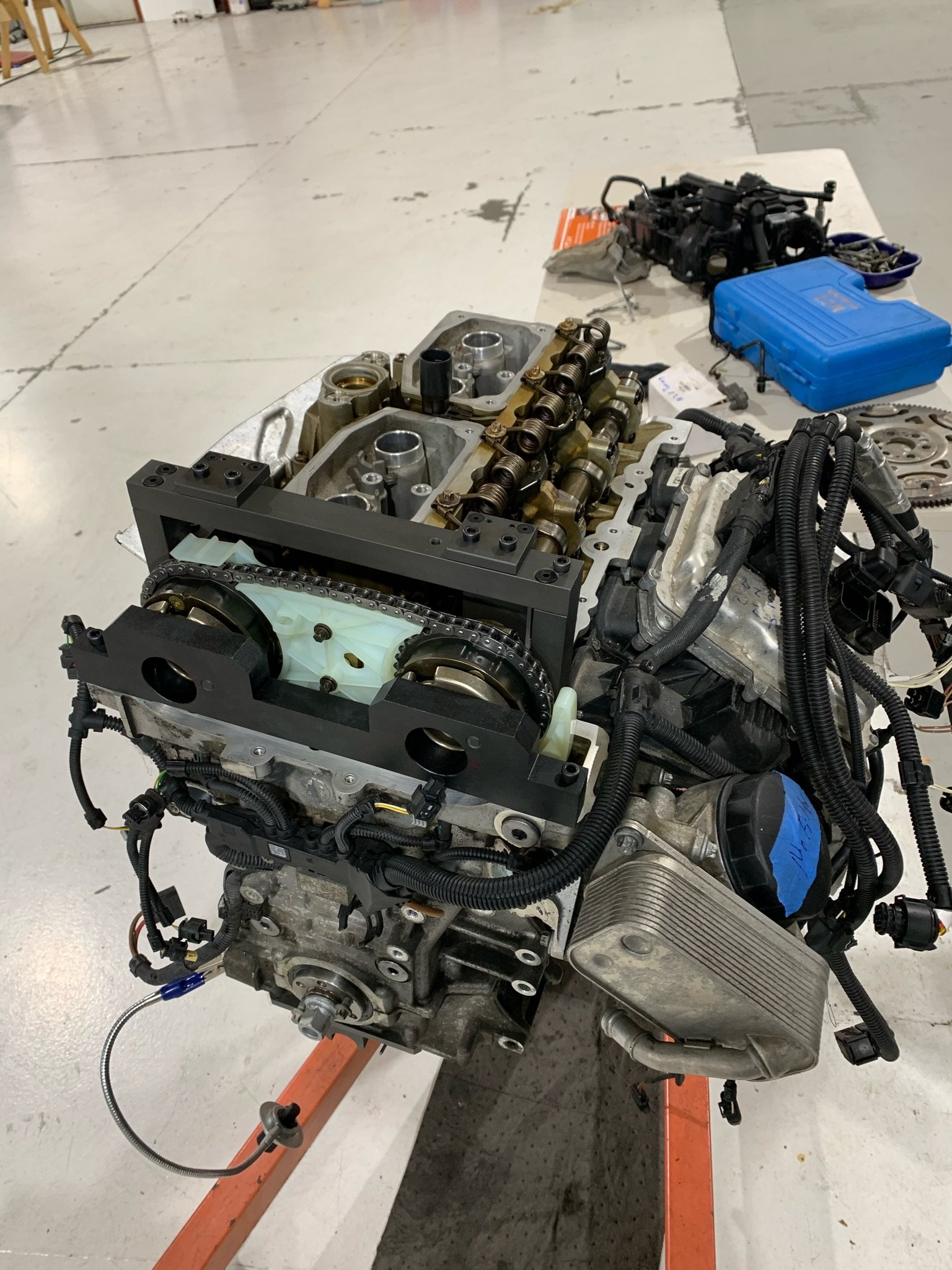 Disassembled car engine placed on an orange stand in a workshop with equipment and tools on the table.