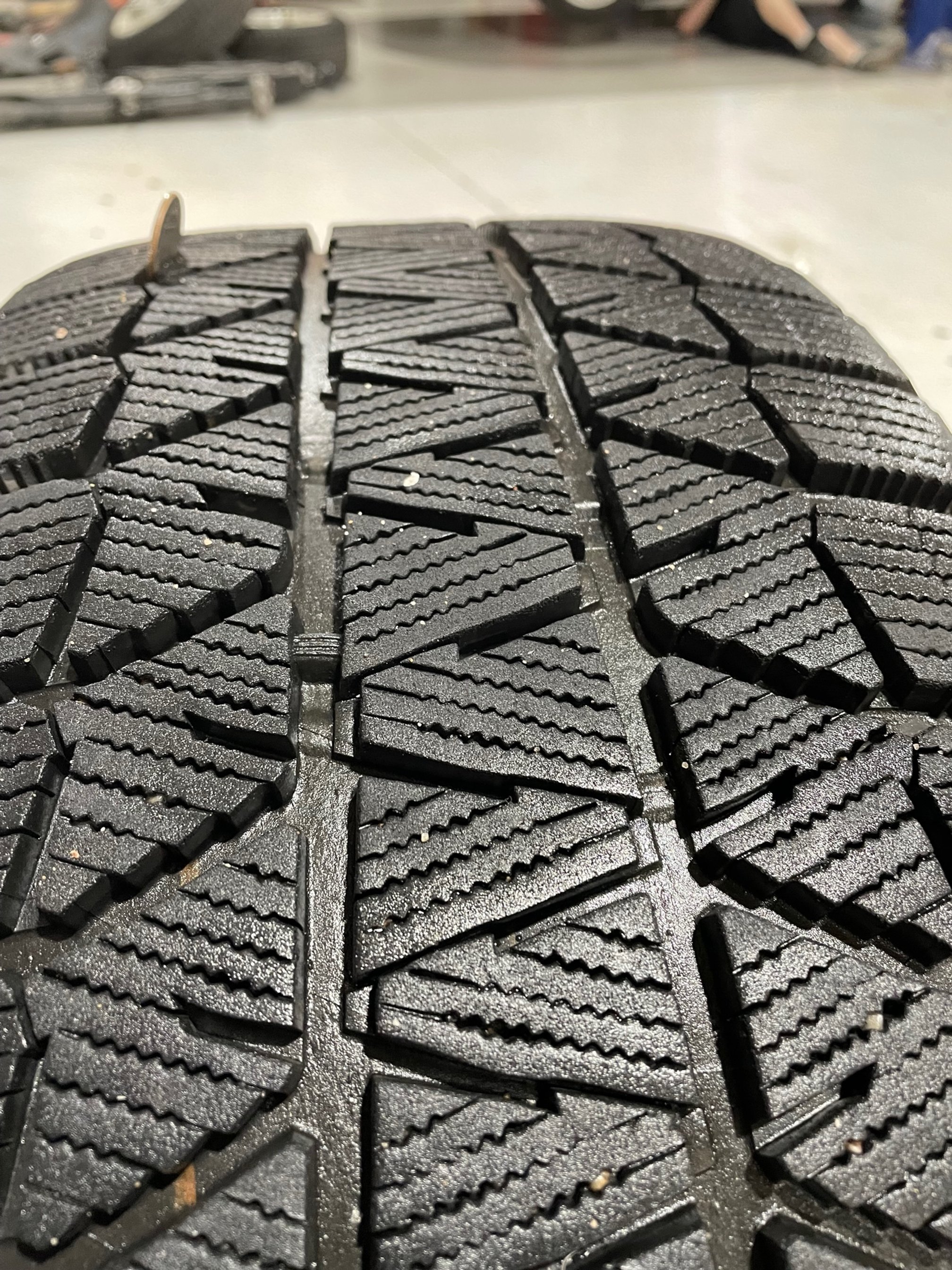 Close-up of a car tire tread, black rubber with detailed zigzag pattern.
