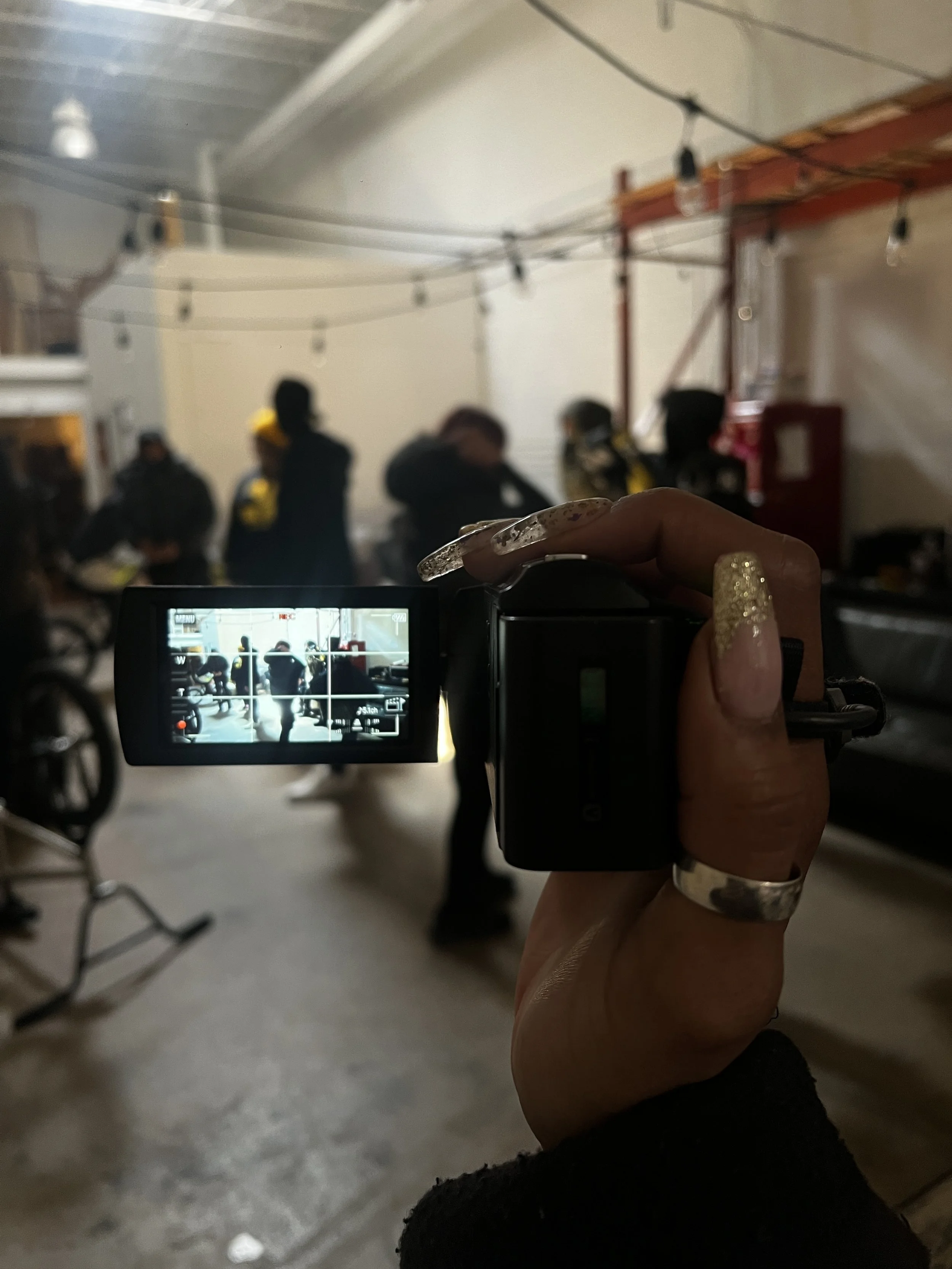 Person holding a camera taking a photo or video of a group of people inside a room, which has string lights hanging from the ceiling and some furniture.