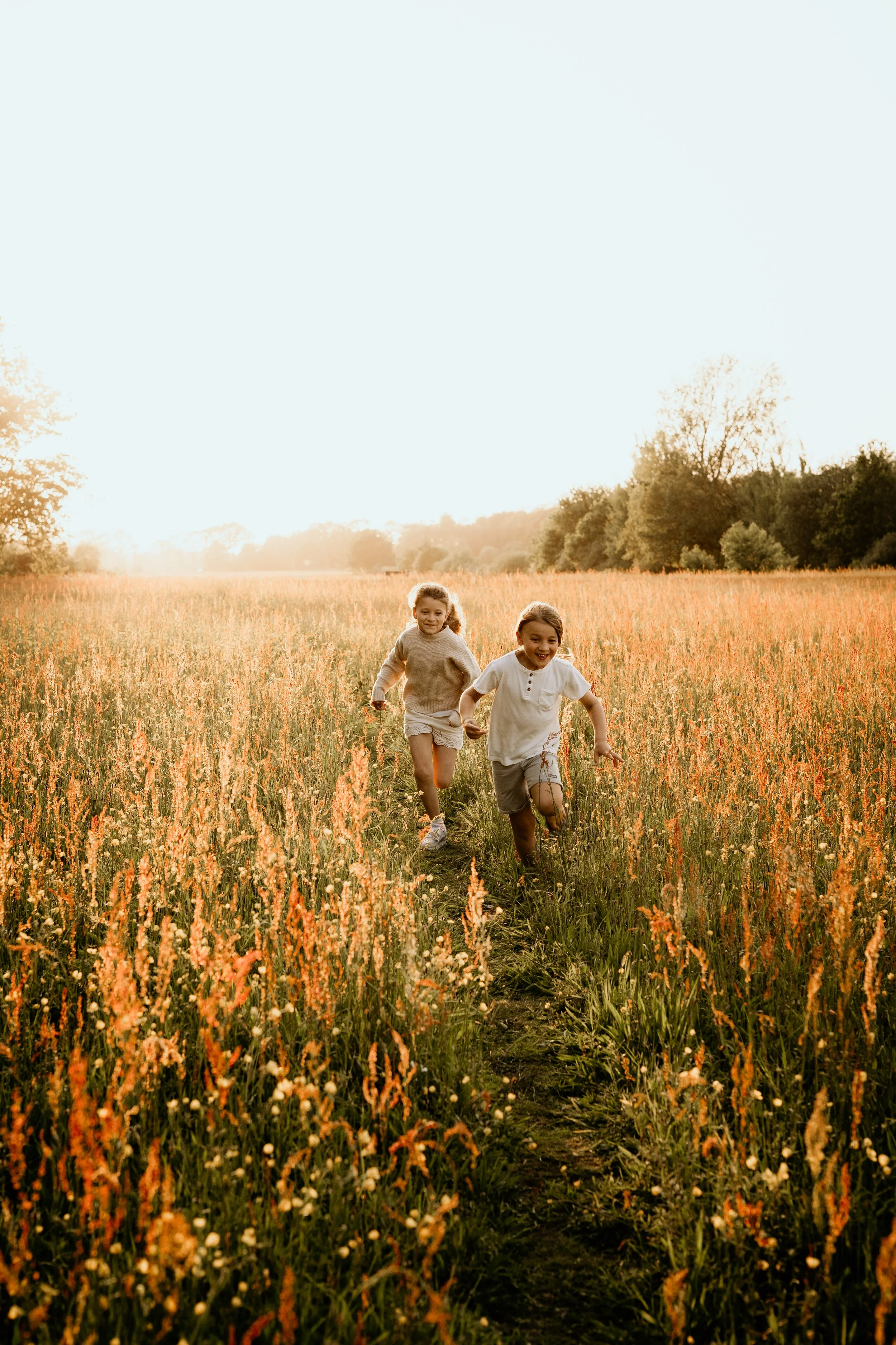 Twee kinderen rennen door het hoge gras, weegbree, in Drenthe met ondergaande zon.