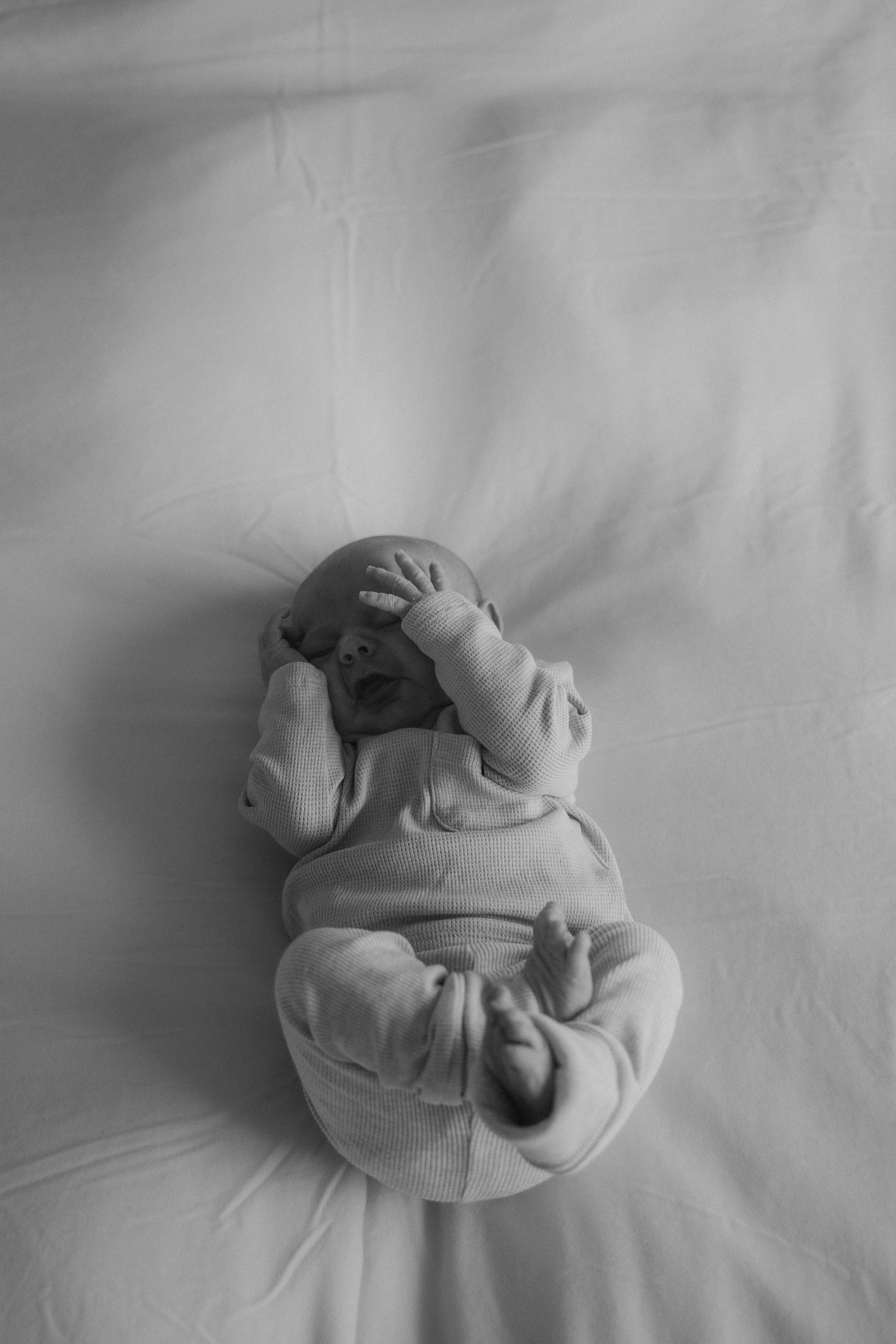 Newborn baby ligt op bed, zwart wit foto.