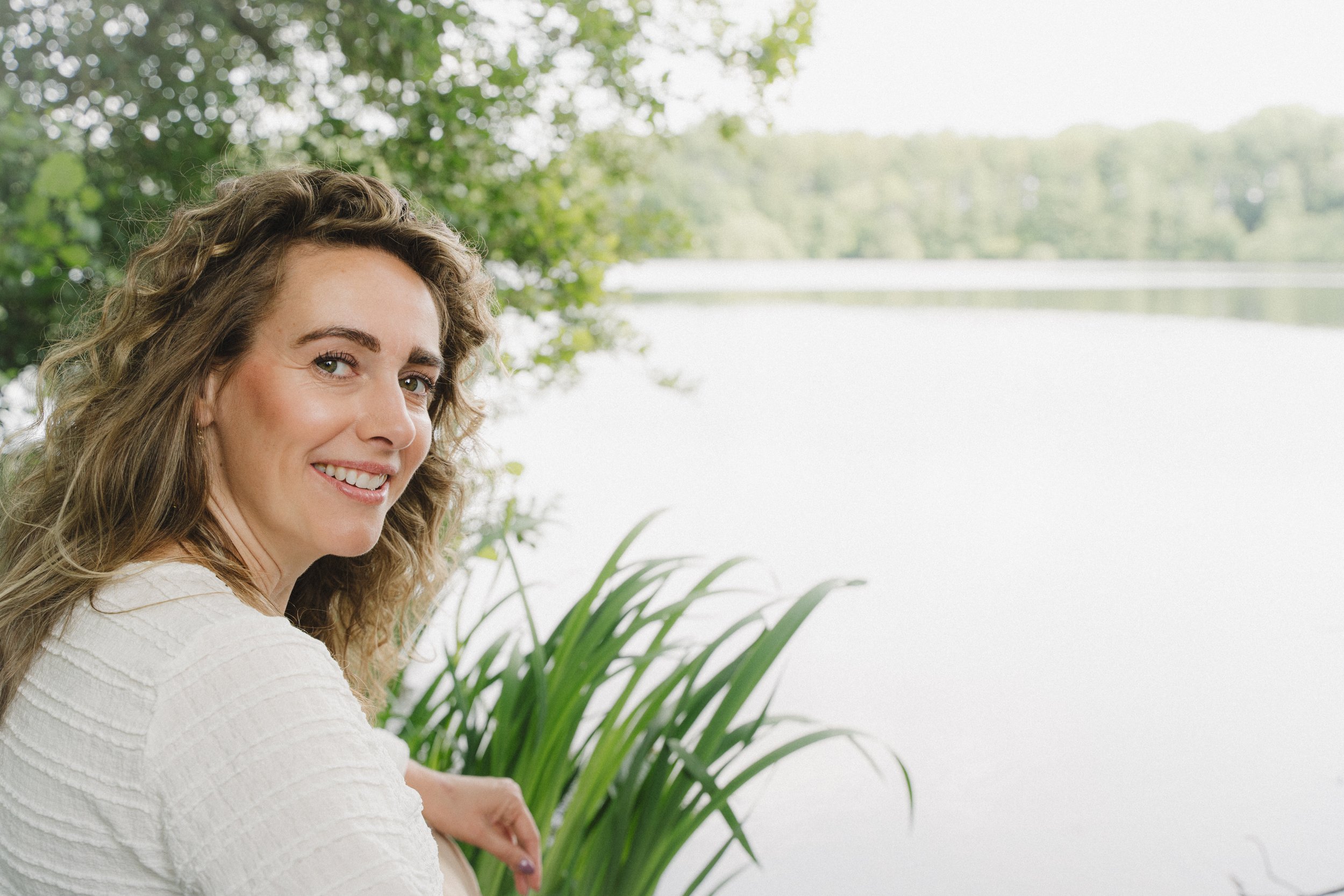 Vrouw zittend aan waterkant kijkt in camera over schouder. Branding, personal branding fotografie.