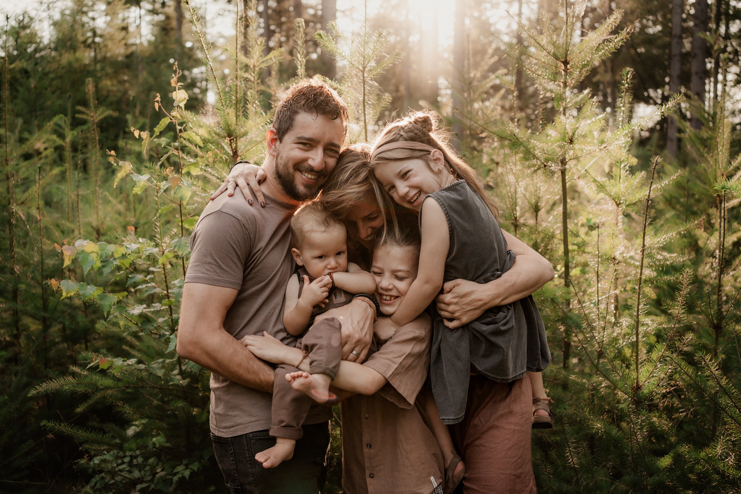 Gezin knuffelend in bosrijke setting met ondergaande zon. Footprint Stories Fotografie, gezinsmoment.