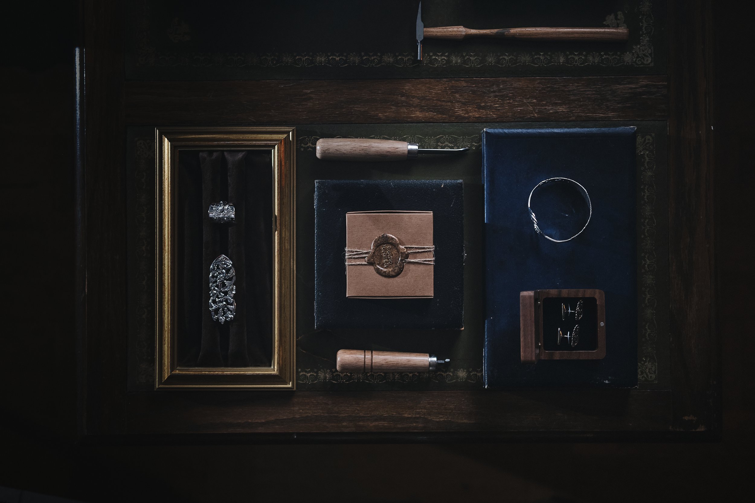A collection of vintage jewelry and accessories including a brooch, cufflinks, a bracelet, and a set of earrings displayed on dark fabric and wooden surfaces.