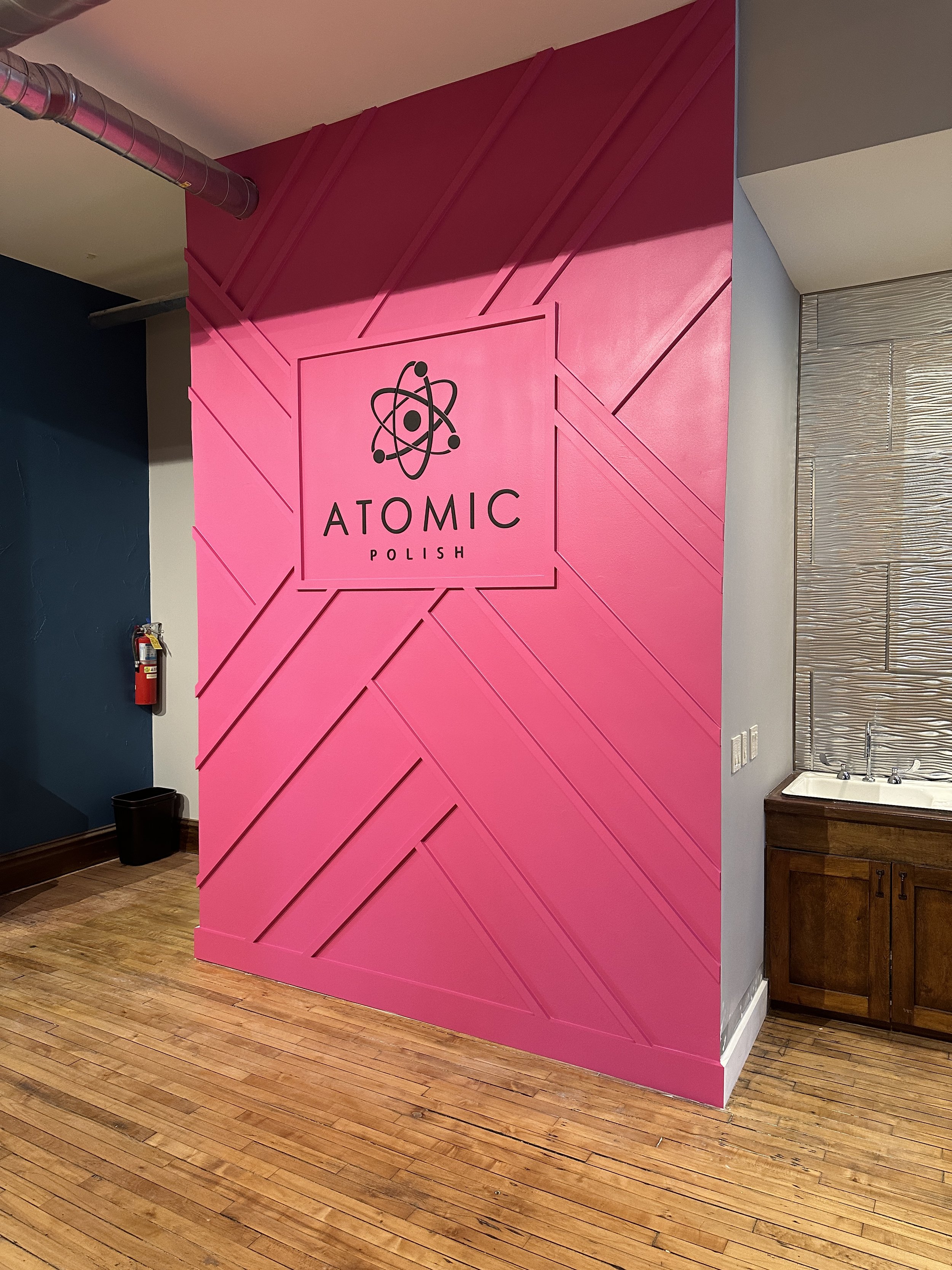 Pink geometric accent wall and logo sign for Atomic Polish.