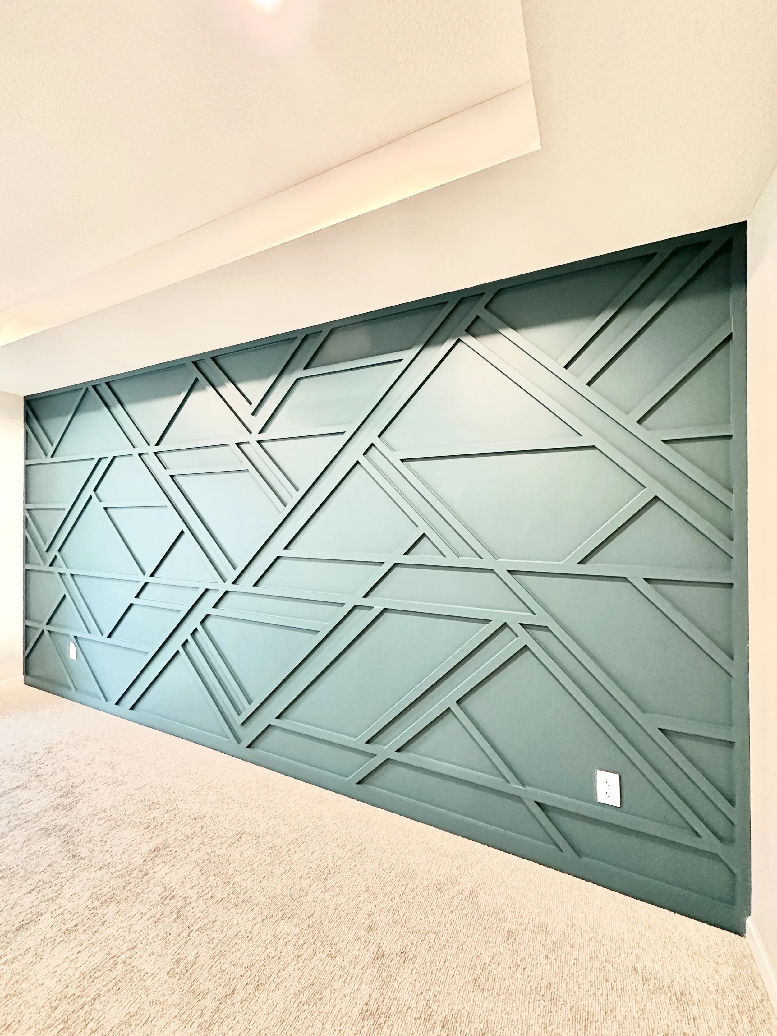 Wall with a geometric pattern made of intersecting lines and shapes painted in teal.