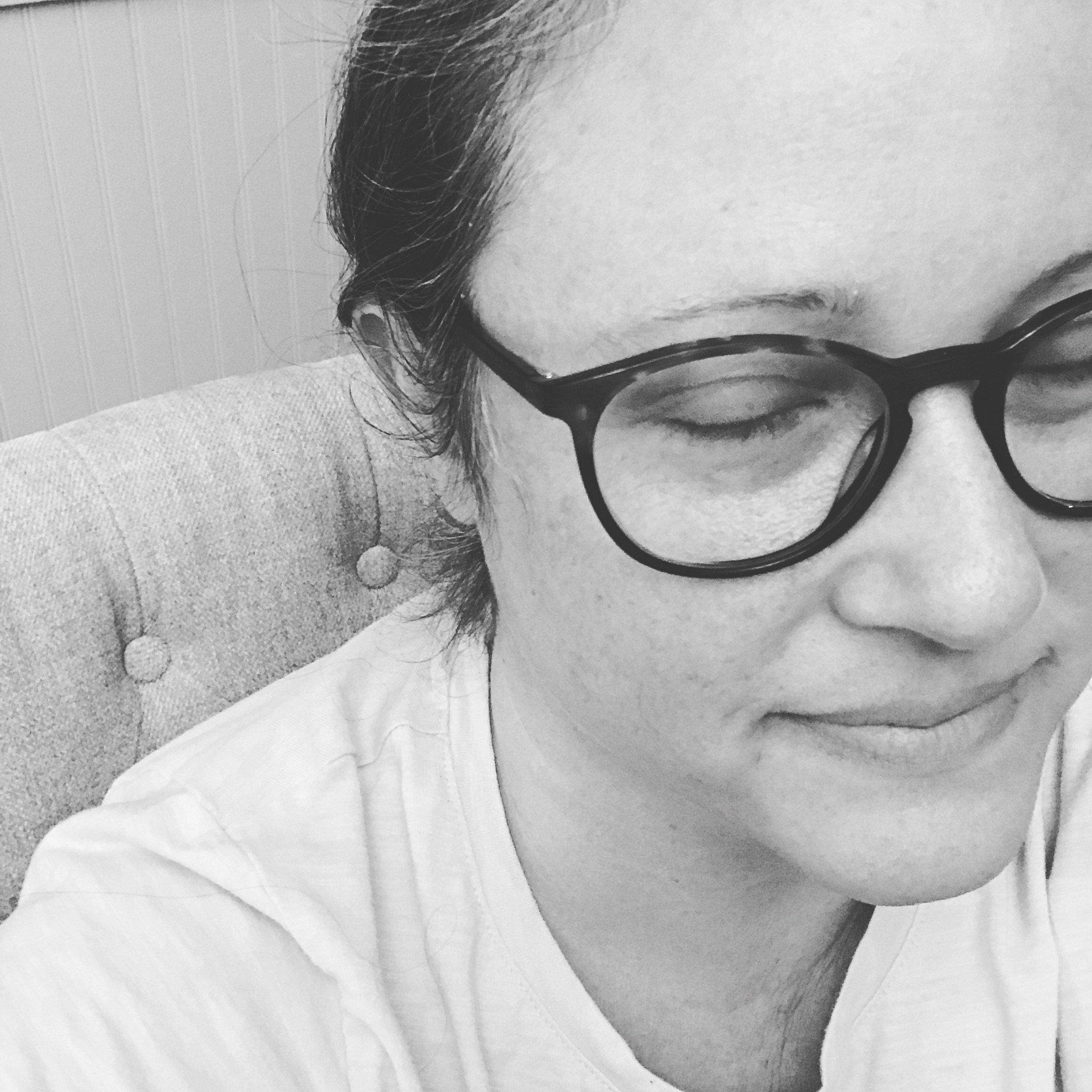 Black and white close-up of a person wearing glasses with eyes closed, smiling slightly, seated on a cushioned chair.