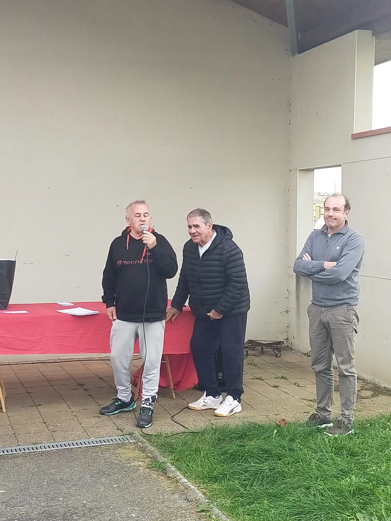 Trois hommes parlent lors d'une réunion en plein air, un d'eux tient un microphone.
