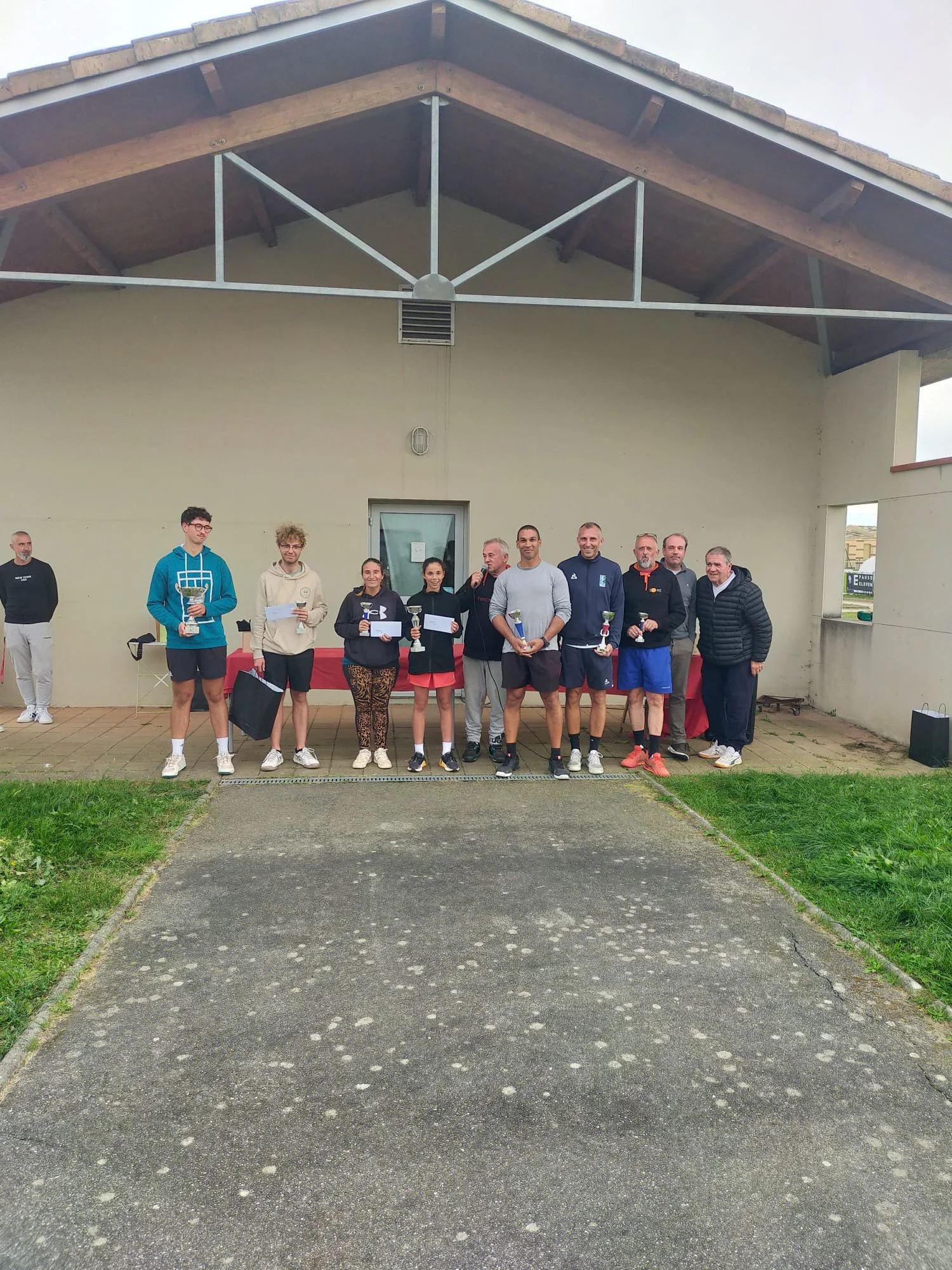 Groupe de personnes lors d'une cérémonie de remise de prix en extérieur, avec une bâche rouge en arrière-plan."