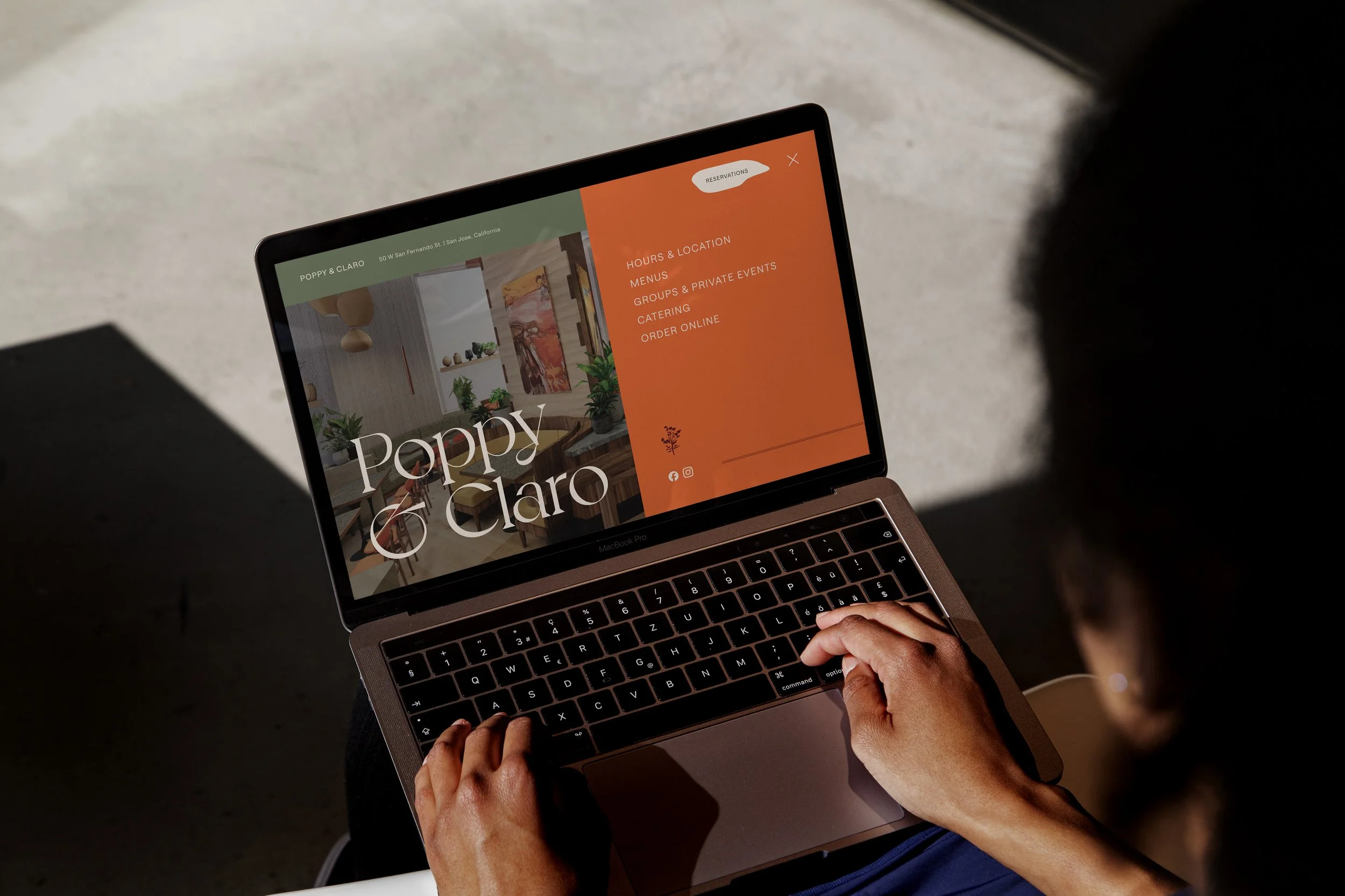 A person using a laptop to view the Poppy & Claro restaurant website design, which features a clean layout, serif typography, and high-quality interior photography.