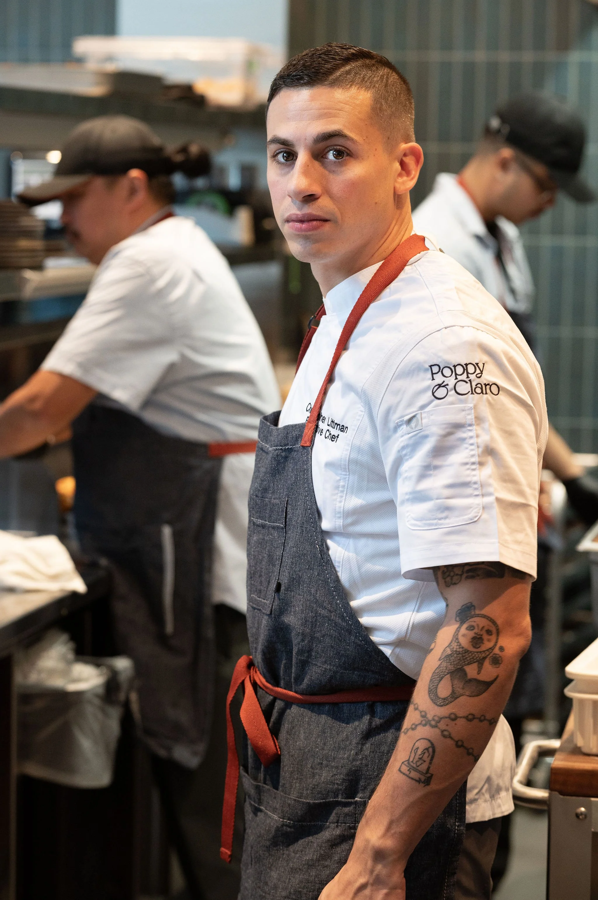 A professional portrait of Executive Chef Christopher Littman in a branded white chef's coat, used in restaurant website design to build personal connection and highlight artisan expertise.