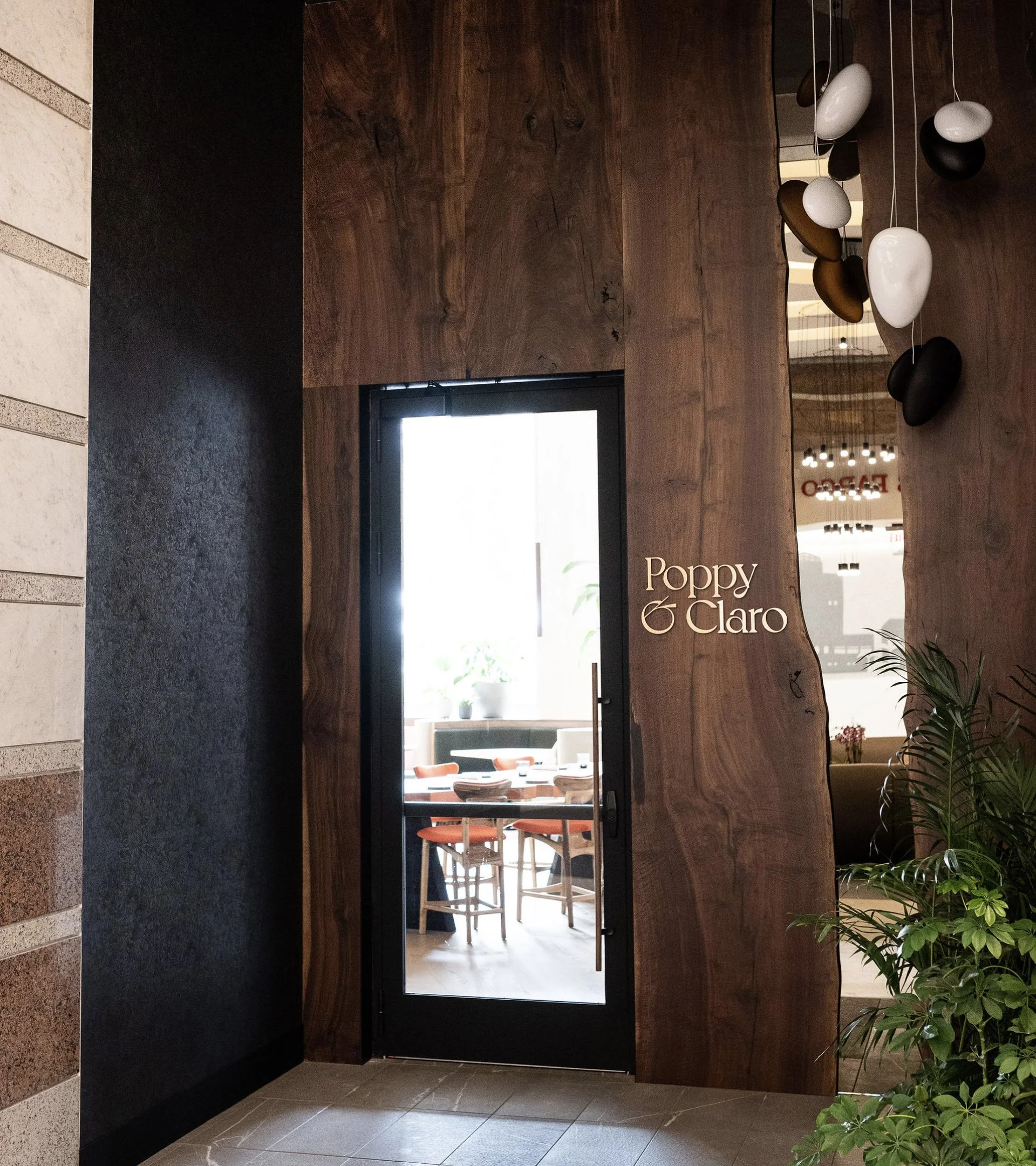 A striking restaurant entrance featured in a restaurant website design, showing a glass door set into a massive, natural-edged dark wood slab with a gold-leaf Poppy & Claro logo.
