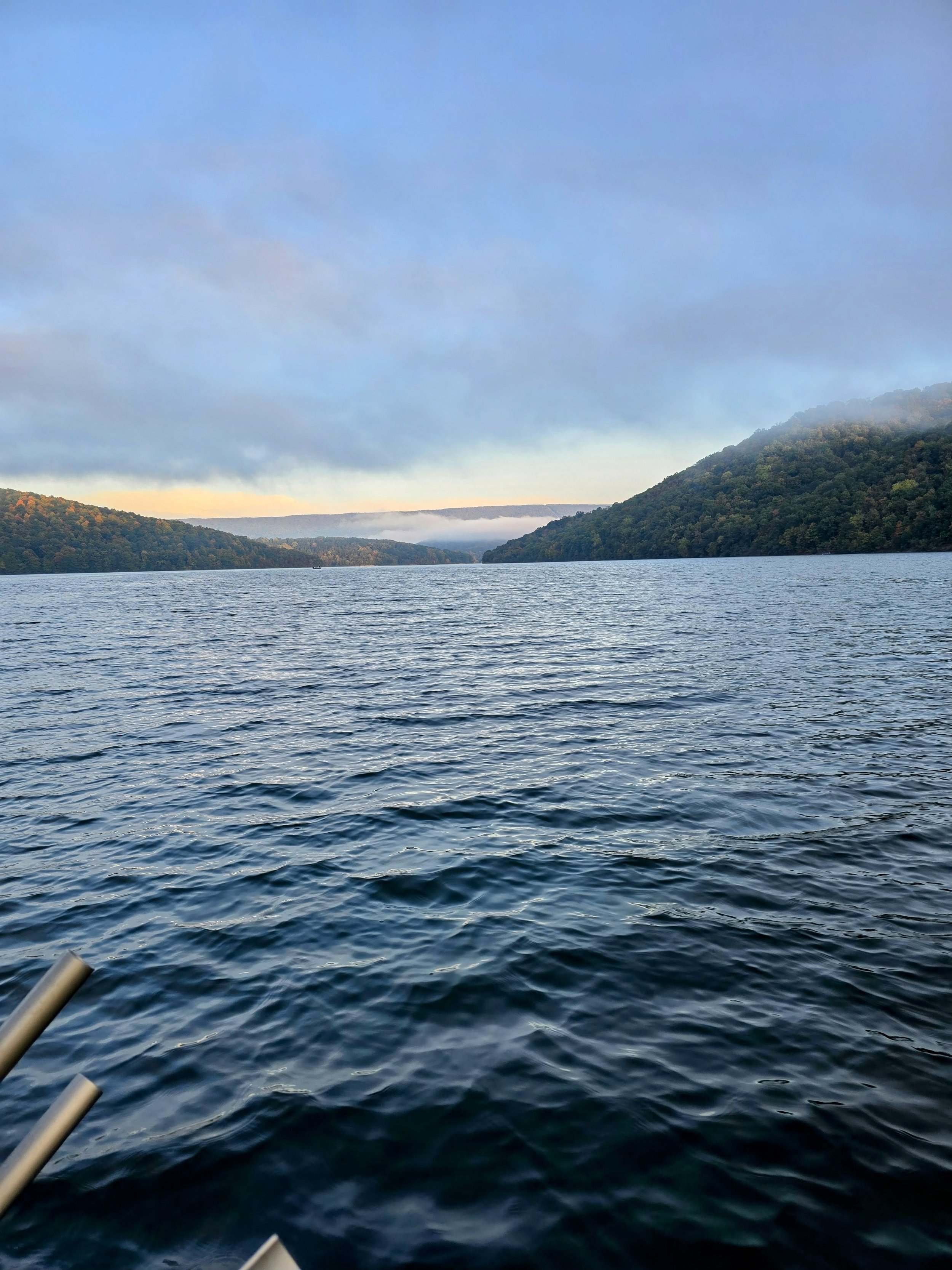 A large body of water surrounded by green forested hills under a partly cloudy sky.