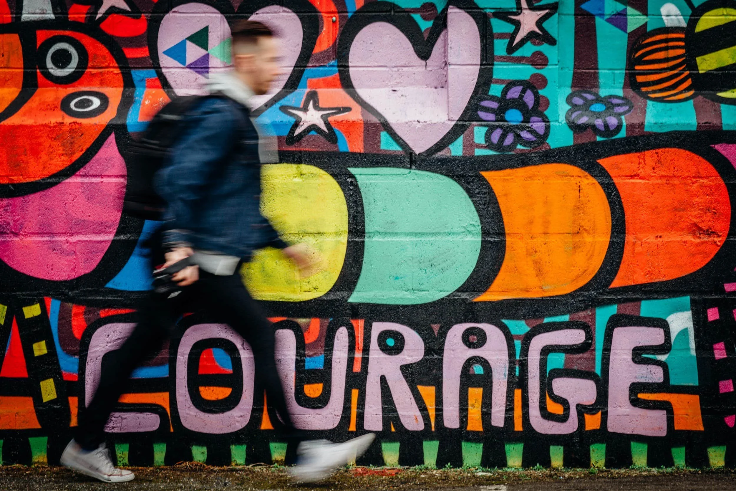 man walking past a mural that says "courage"
