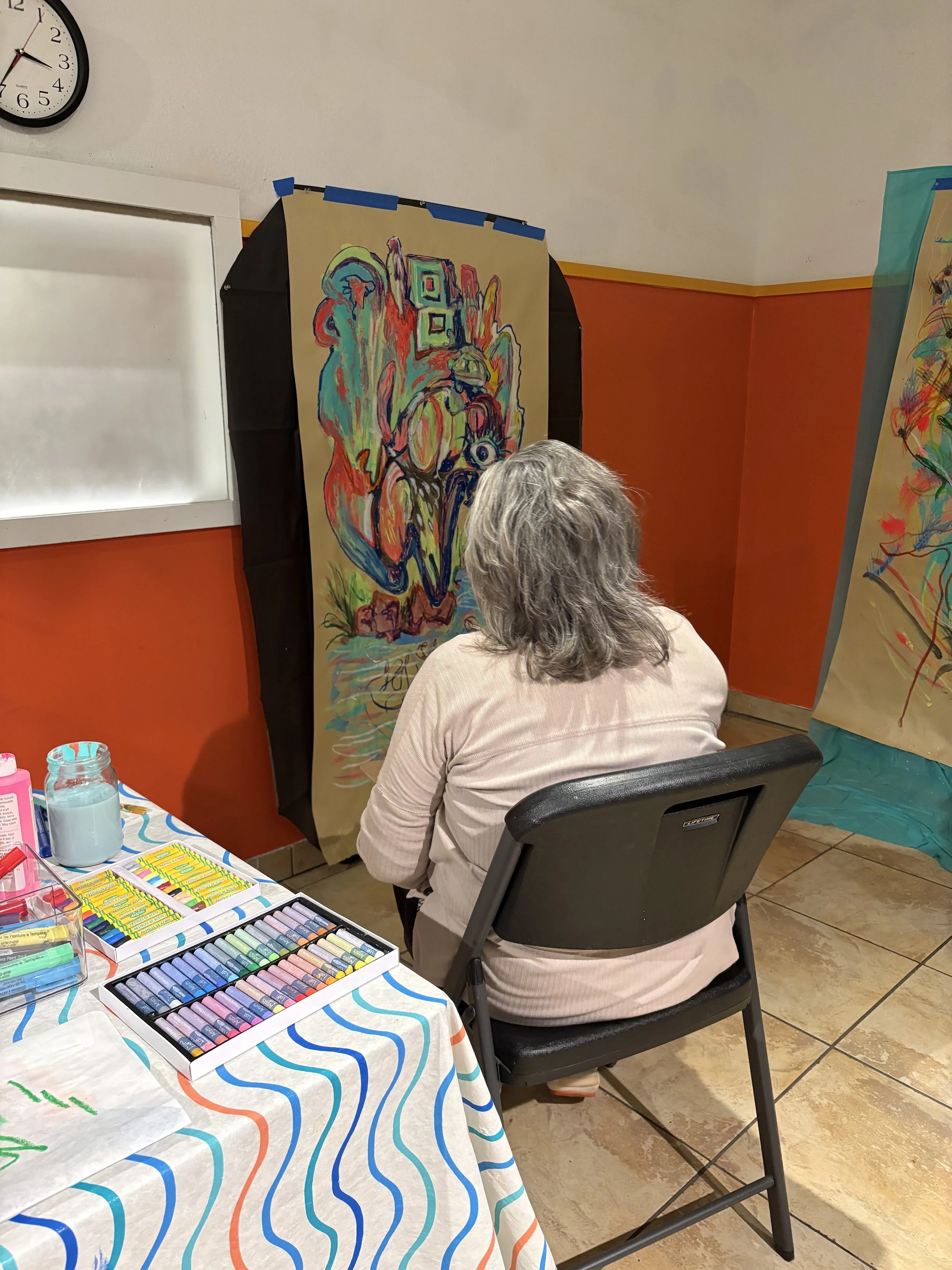 Participant working on a large-scale mixed media drawing during ArtFull Thursdays at Manitou Art Center, with colorful pastel sets on the table.