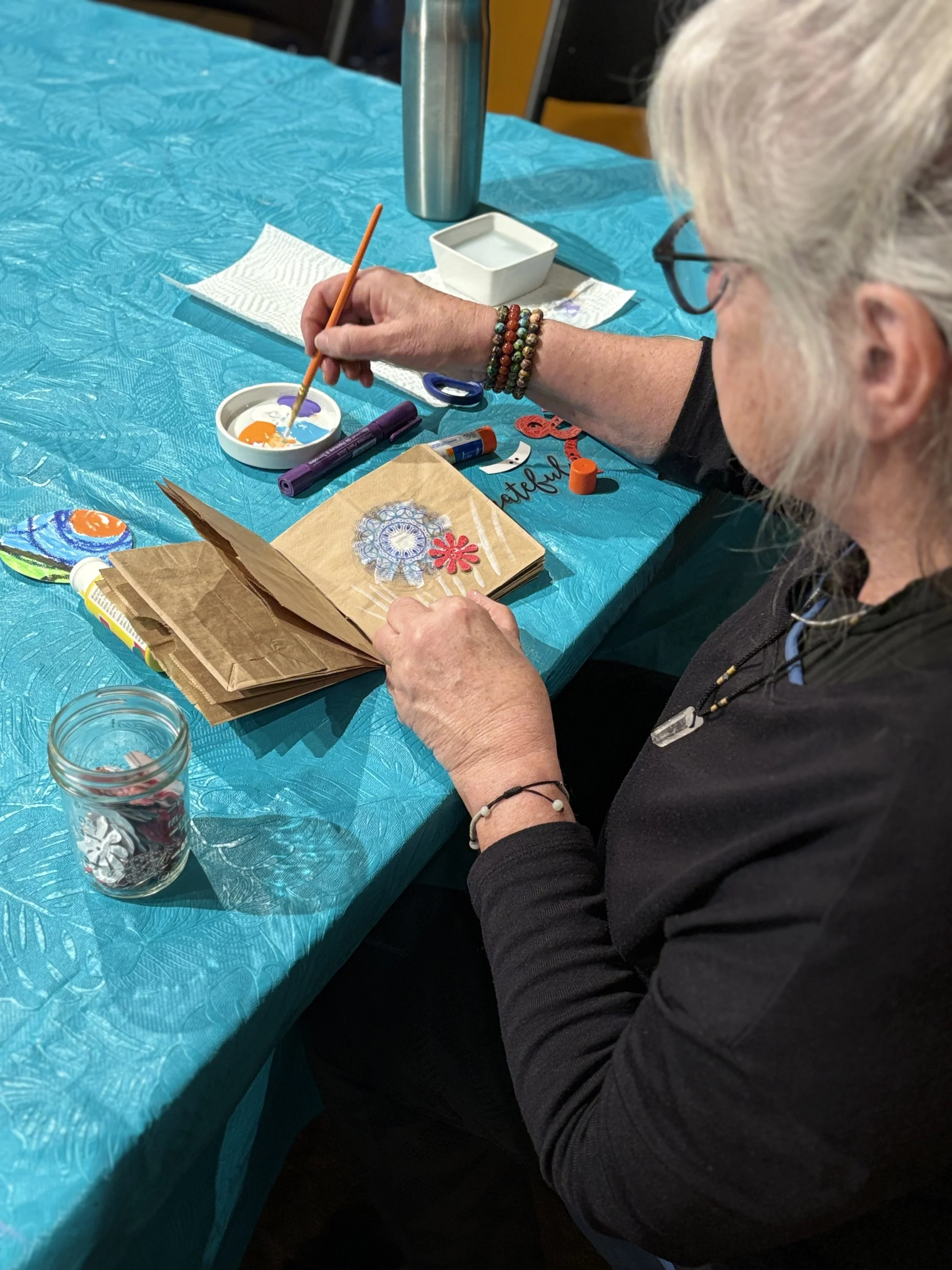 Participant painting a design in a handmade art journal during ArtFull Thursdays, a restorative expressive arts gathering for adults in Manitou Springs, CO.