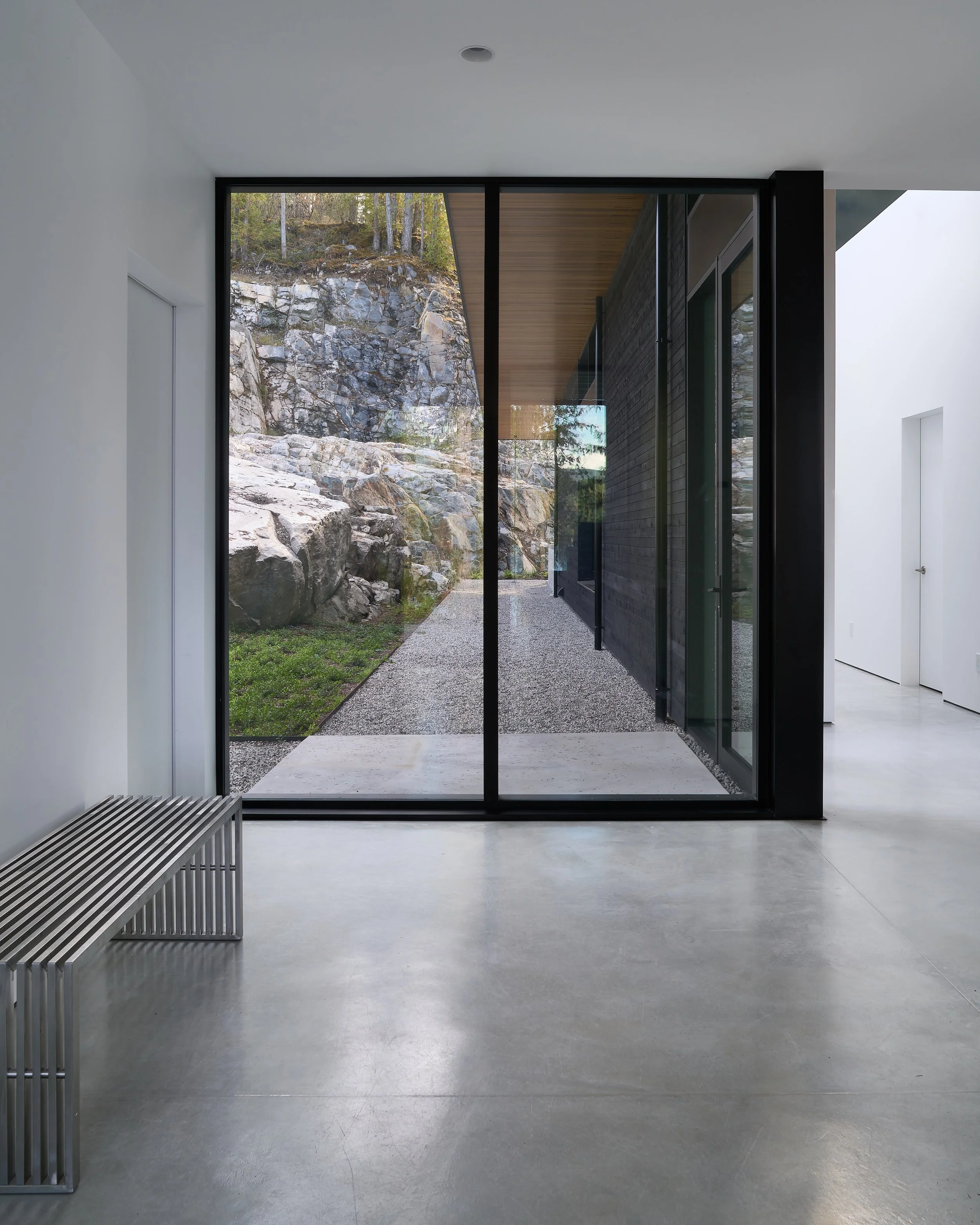 Modern interior room with large glass sliding doors showing rocky outdoor landscape with trees.