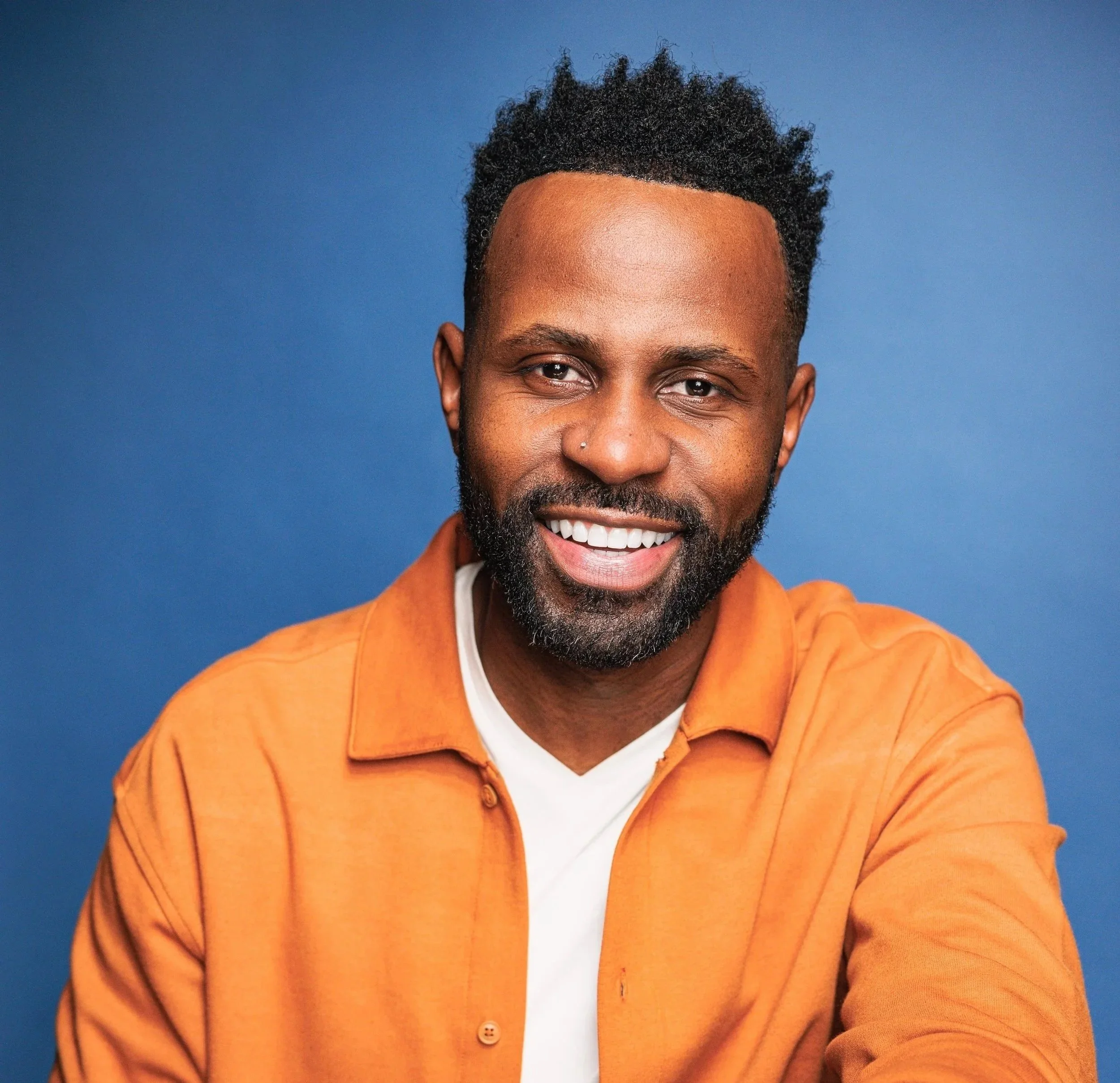 Justin D. Key smiling in a colorful shirt against a blue background.