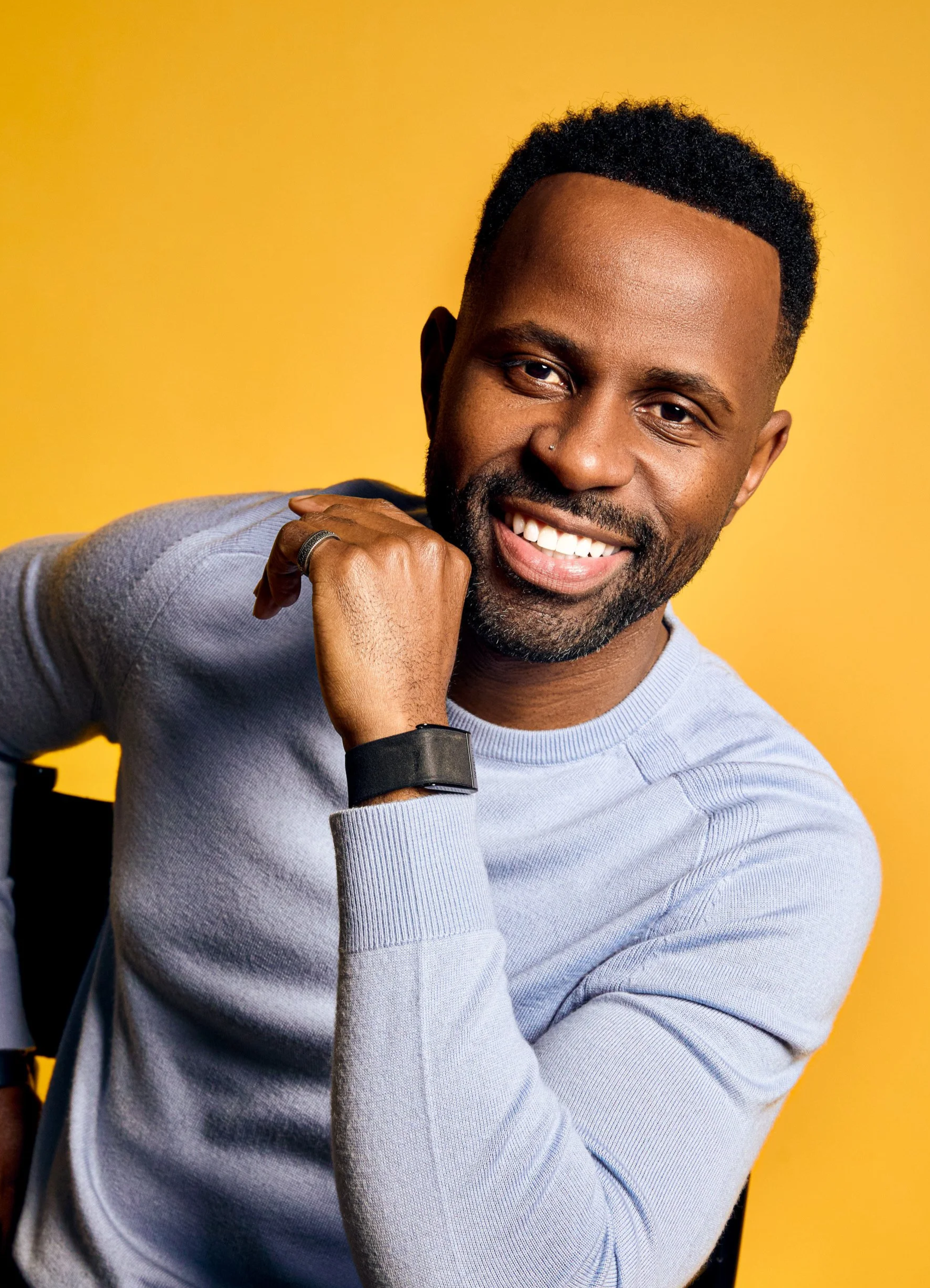 Justin D. Key smiling in a light blue sweater against a yellow background.