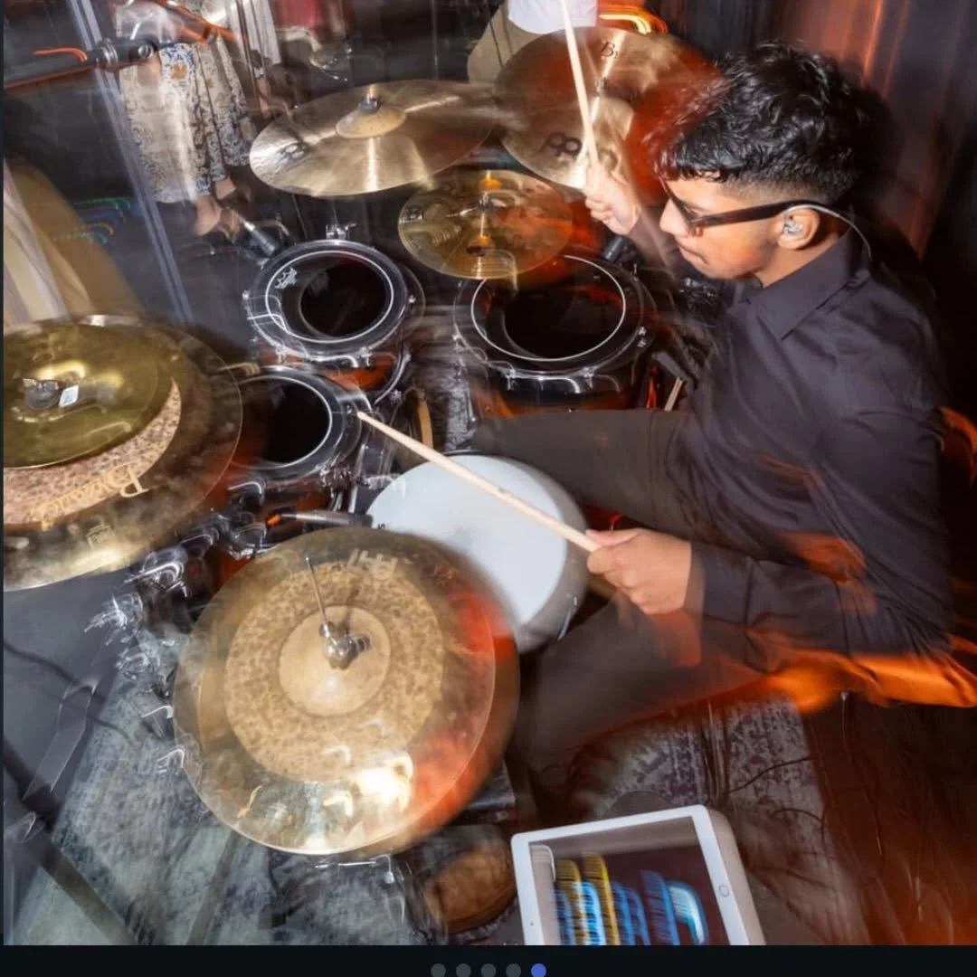A young man playing a drum set consisting of cymbals and drums in a music studio or room, with motion blur indicating vigorous movement.