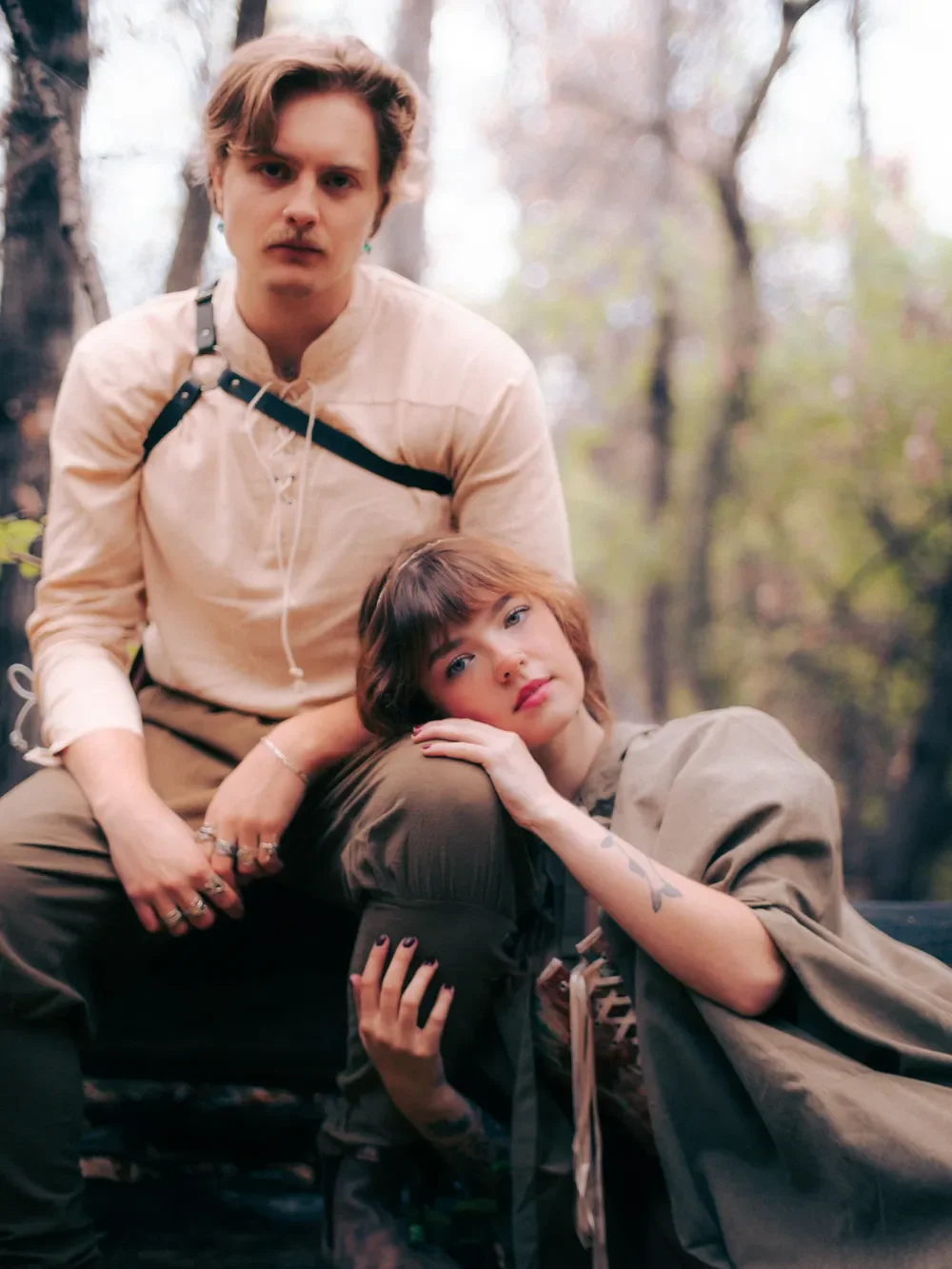 A masc and a feme person lean against each other in a forest.